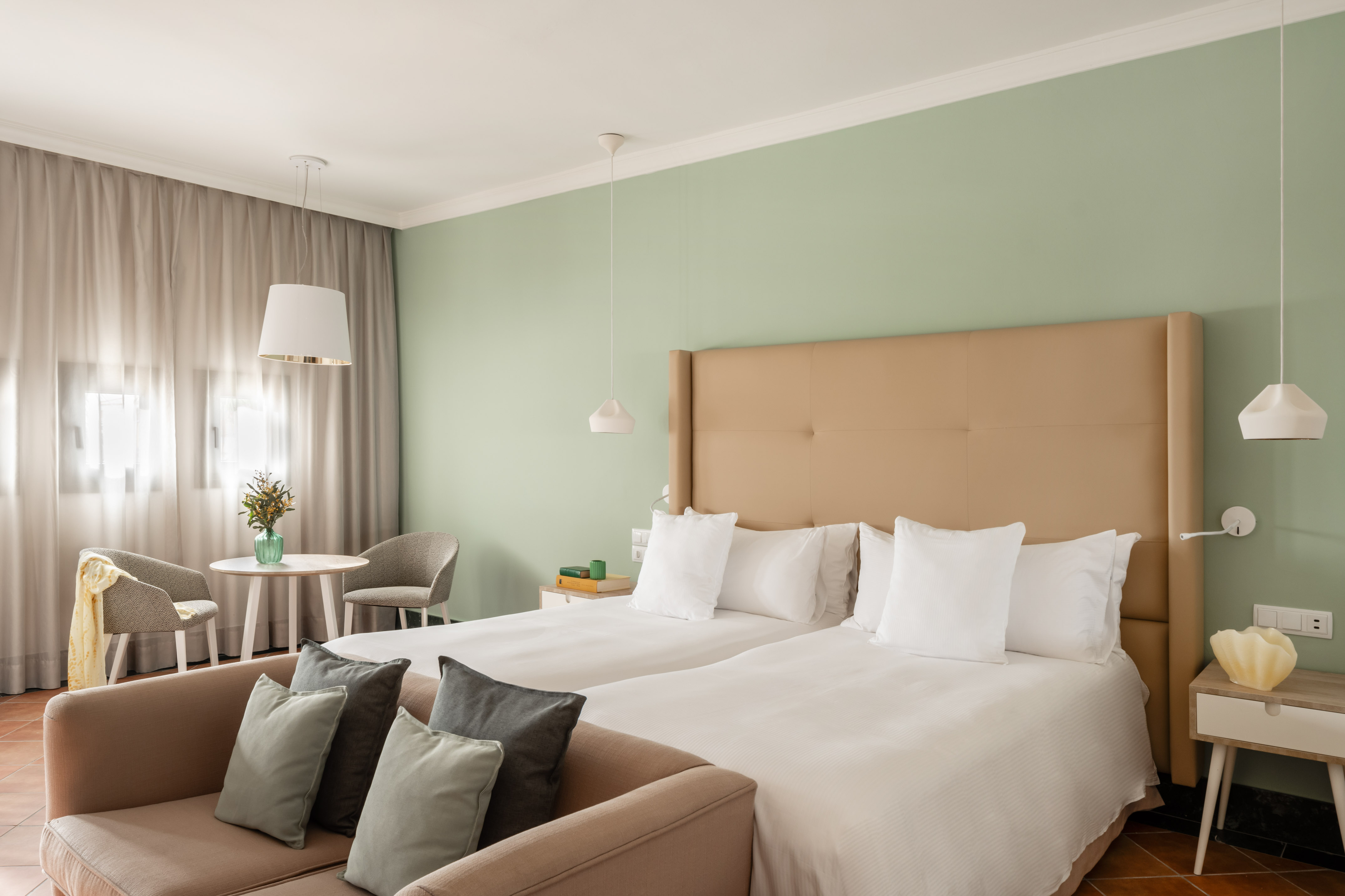 Modern hotel room with twin beds, green accent wall, and a sitting area.