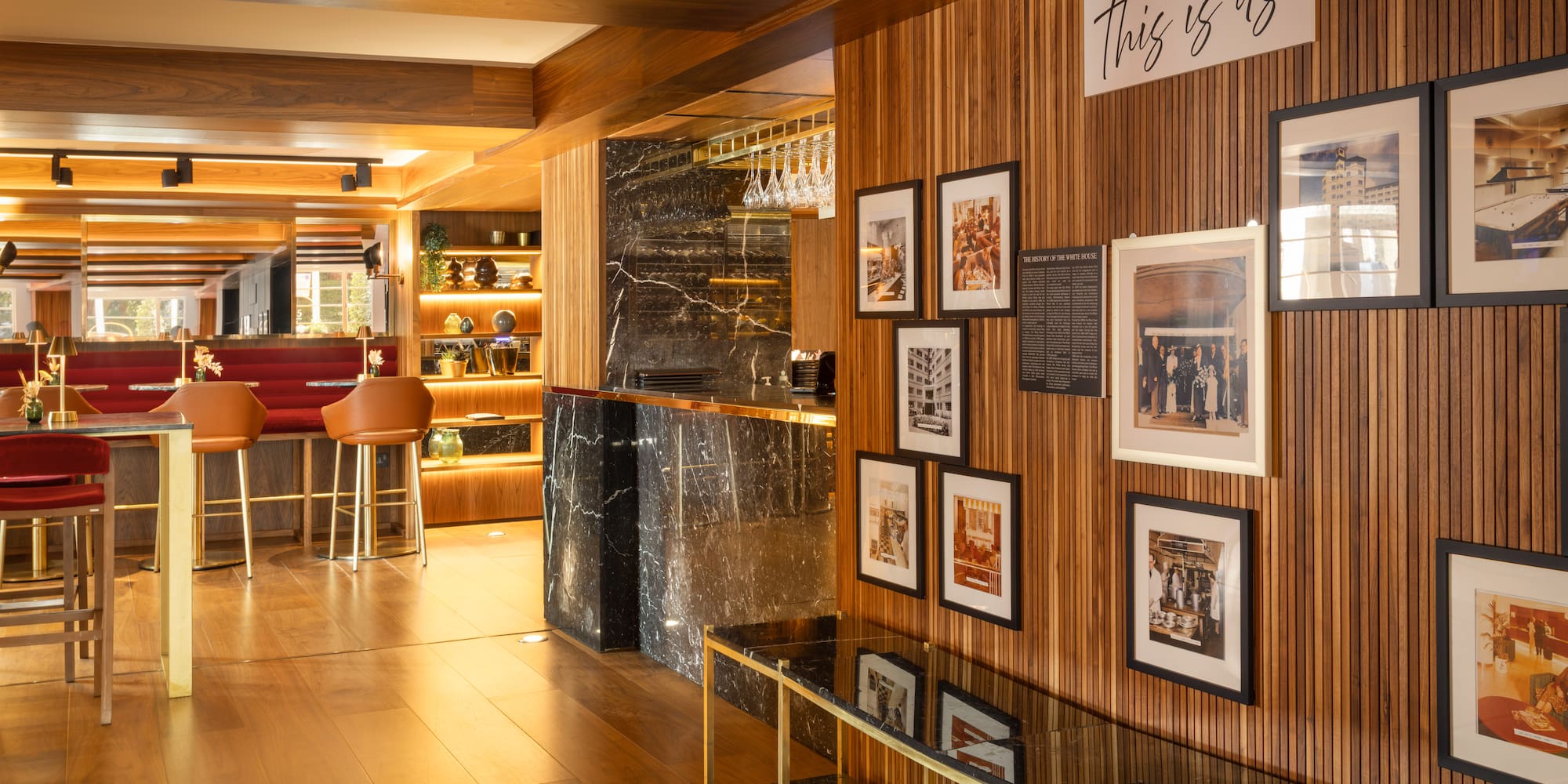 Elegant hotel bar: wood paneling, marble counter, red seating, historic photos.