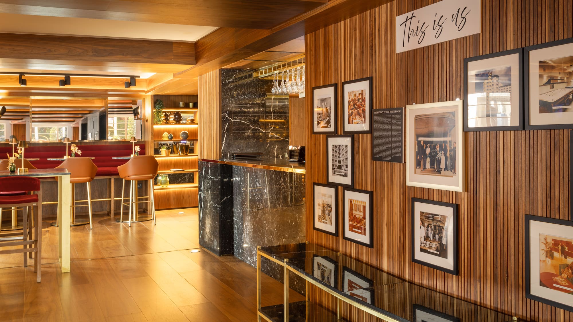 Elegant hotel bar: wood paneling, marble counter, red seating, historic photos.