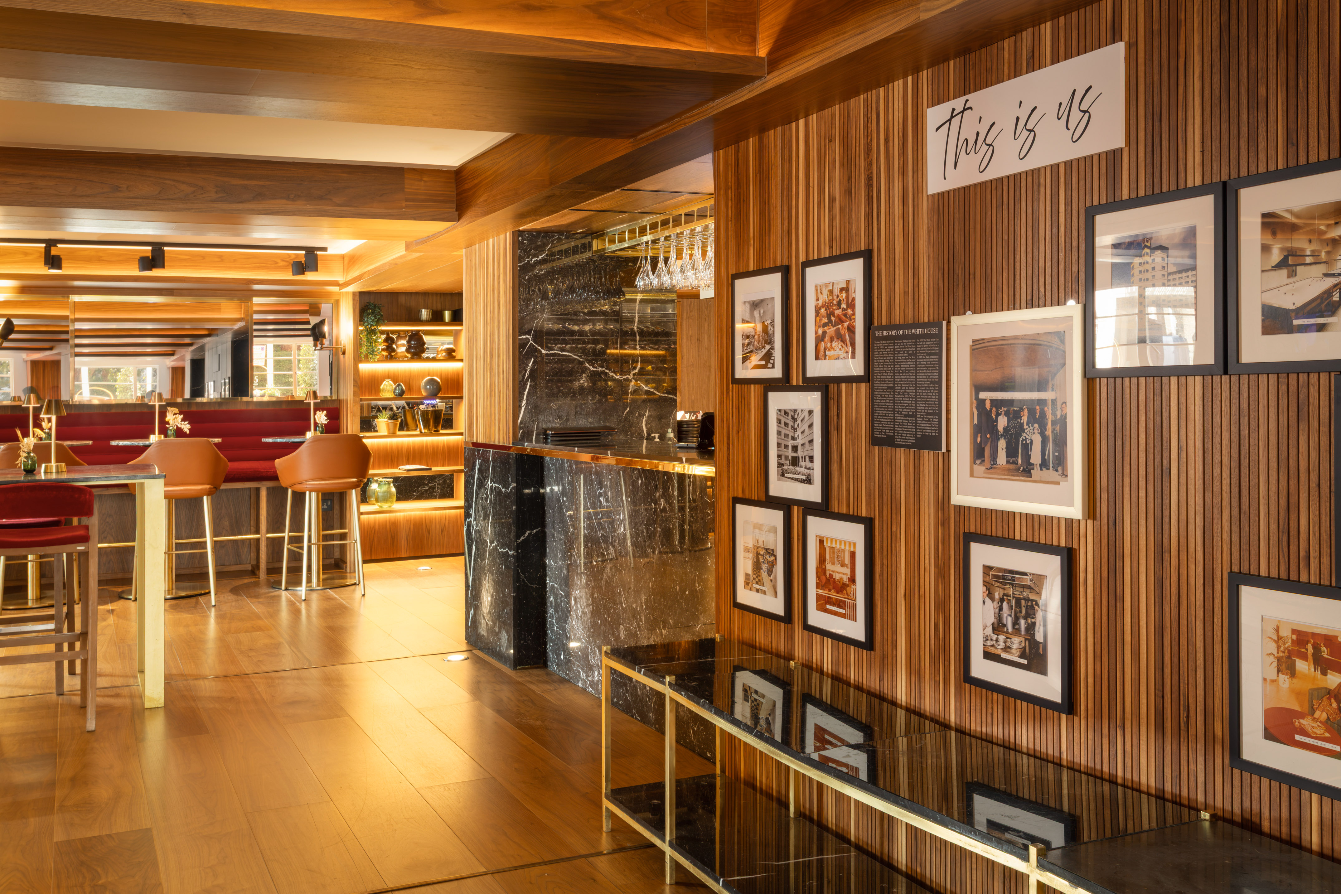Elegant hotel bar: wood paneling, marble counter, red seating, historic photos.