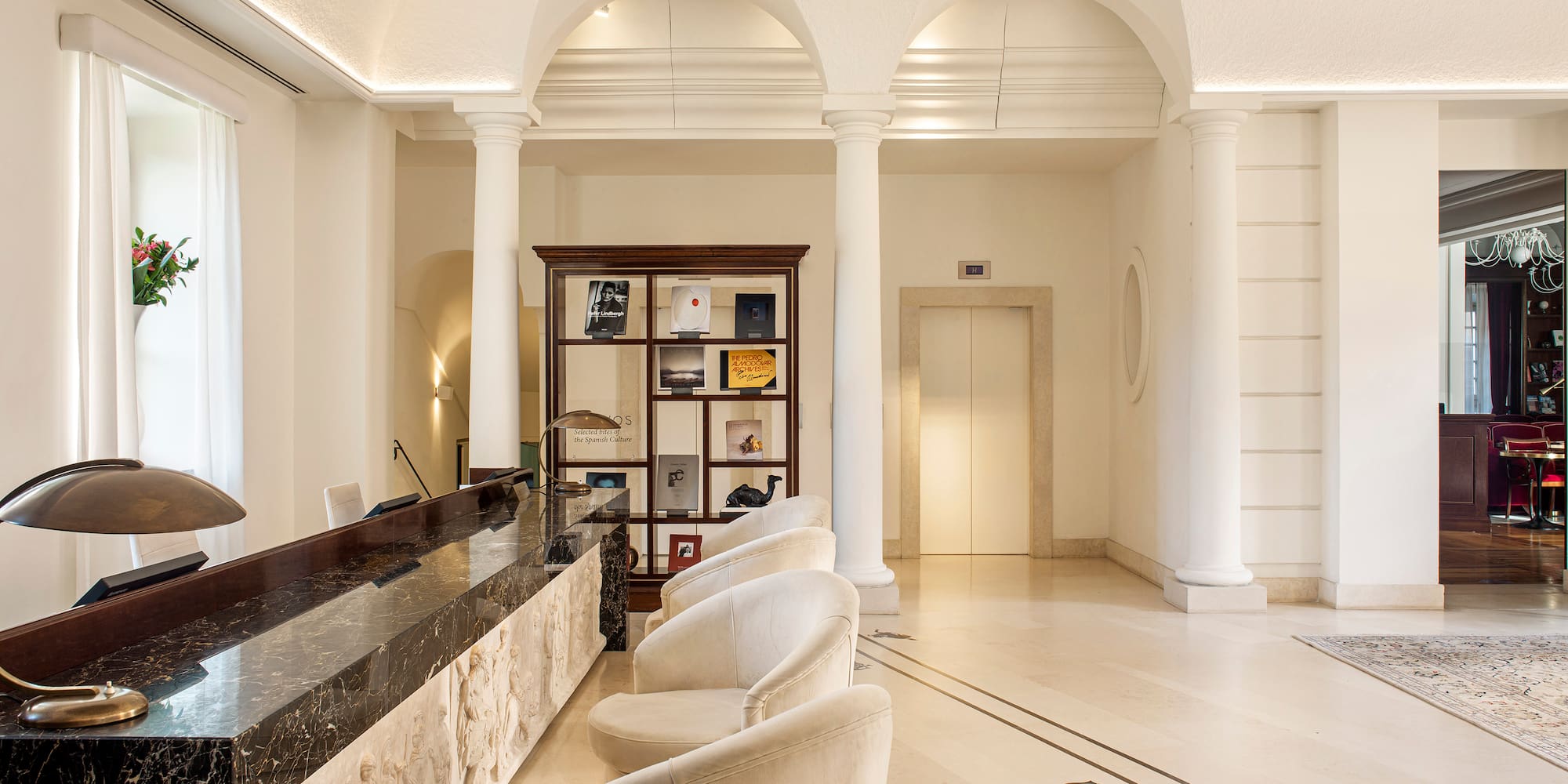 Classic hotel lobby reception with marble desk, arches, and white chairs.