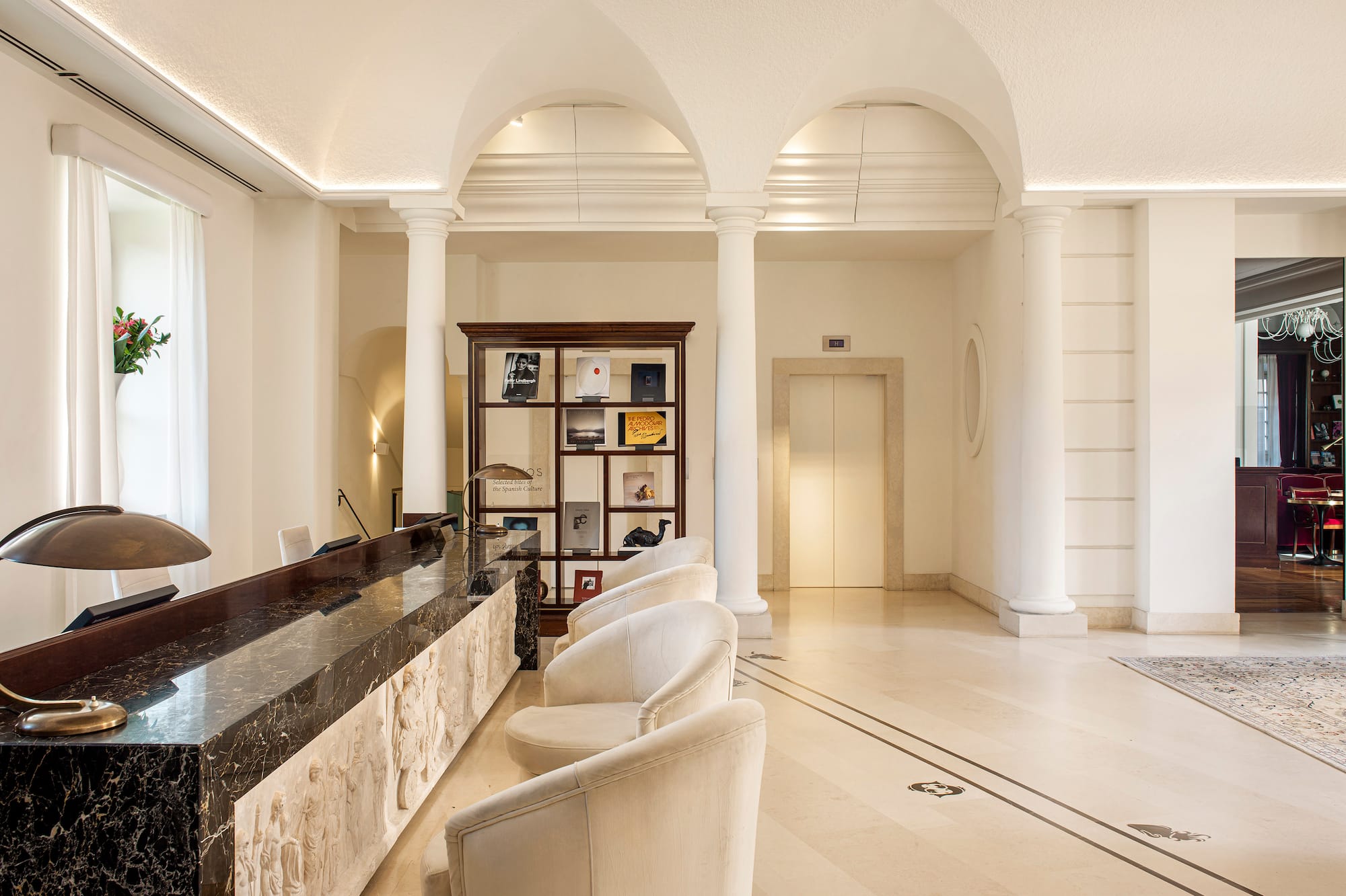 Classic hotel lobby reception with marble desk, arches, and white chairs.