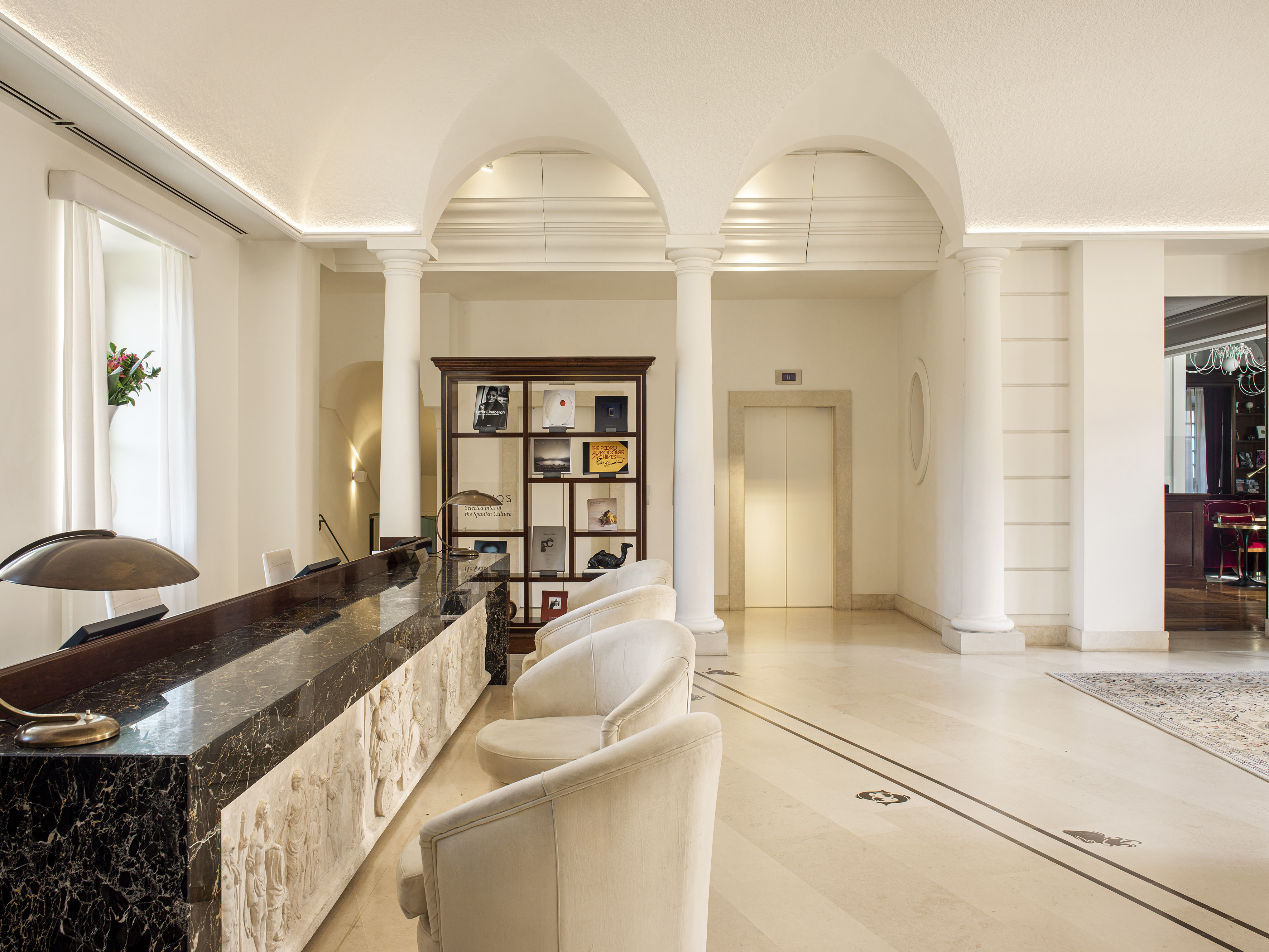 Classic hotel lobby reception with marble desk, arches, and white chairs.