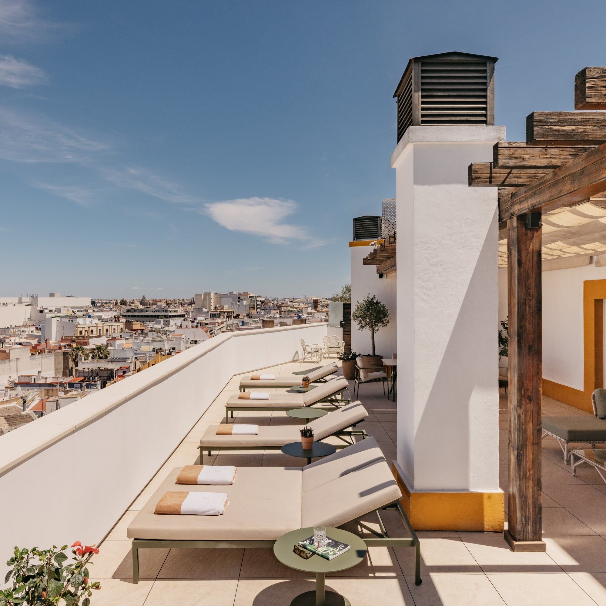 Azotea mediterránea con tumbonas, pérgola de madera y vistas urbanas soleadas.
