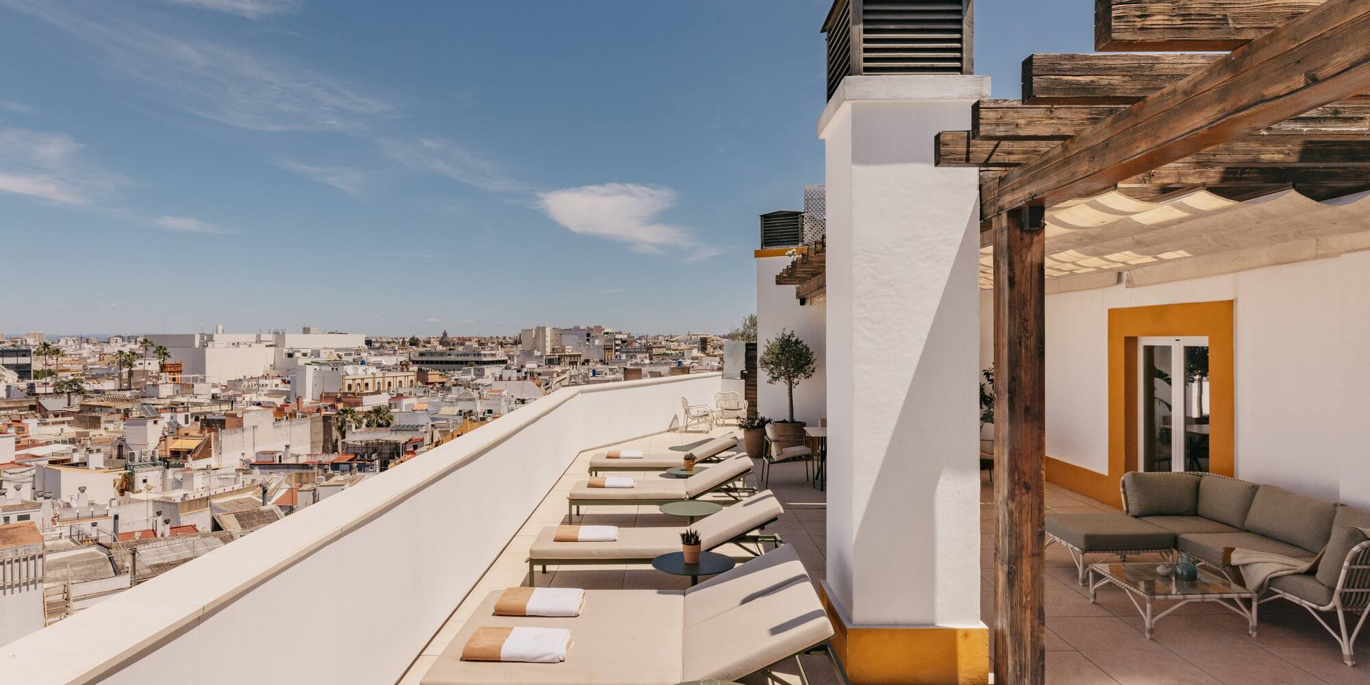 Azotea mediterránea con tumbonas, pérgola de madera y vistas urbanas soleadas.
