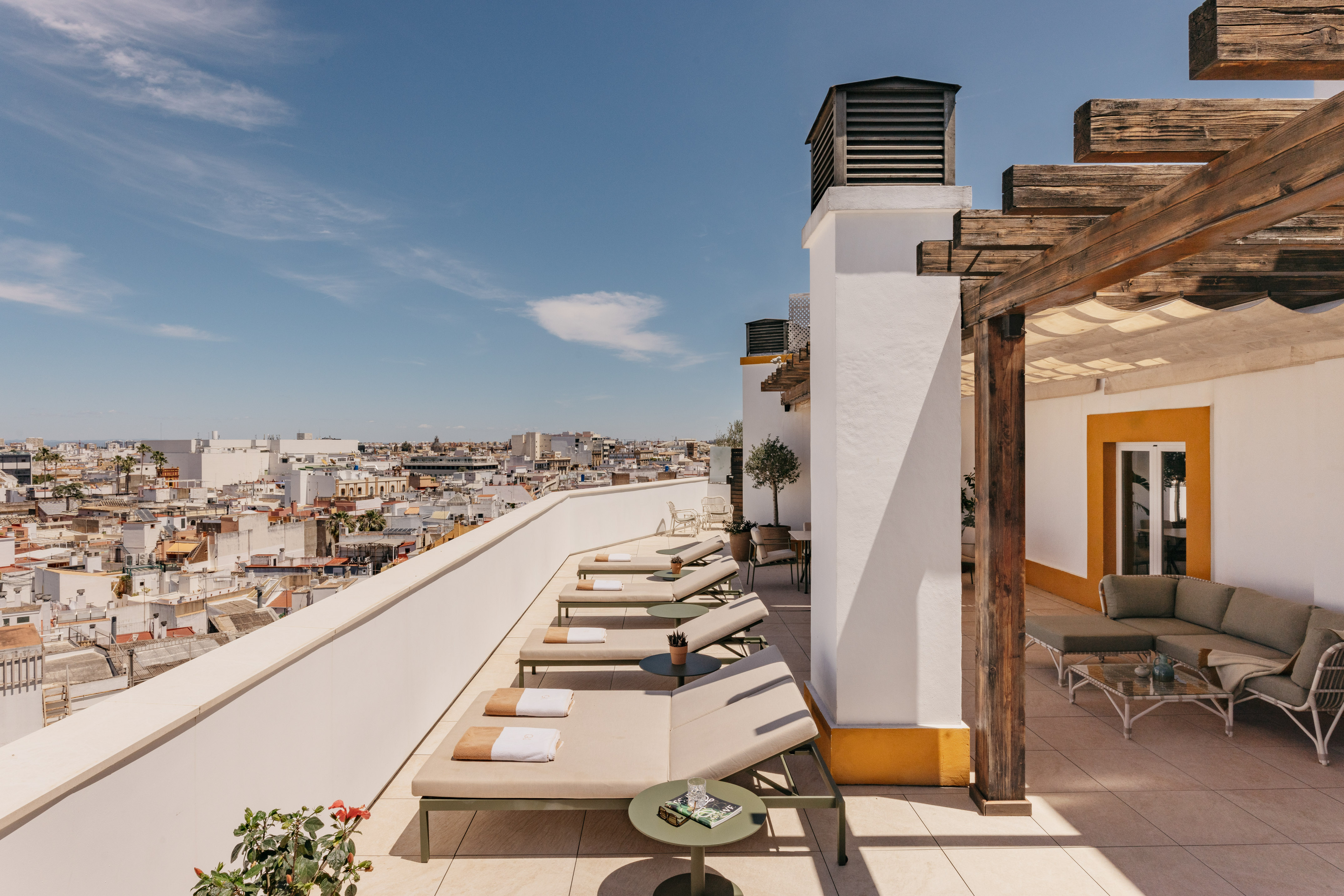 Azotea mediterránea con tumbonas, pérgola de madera y vistas urbanas soleadas.