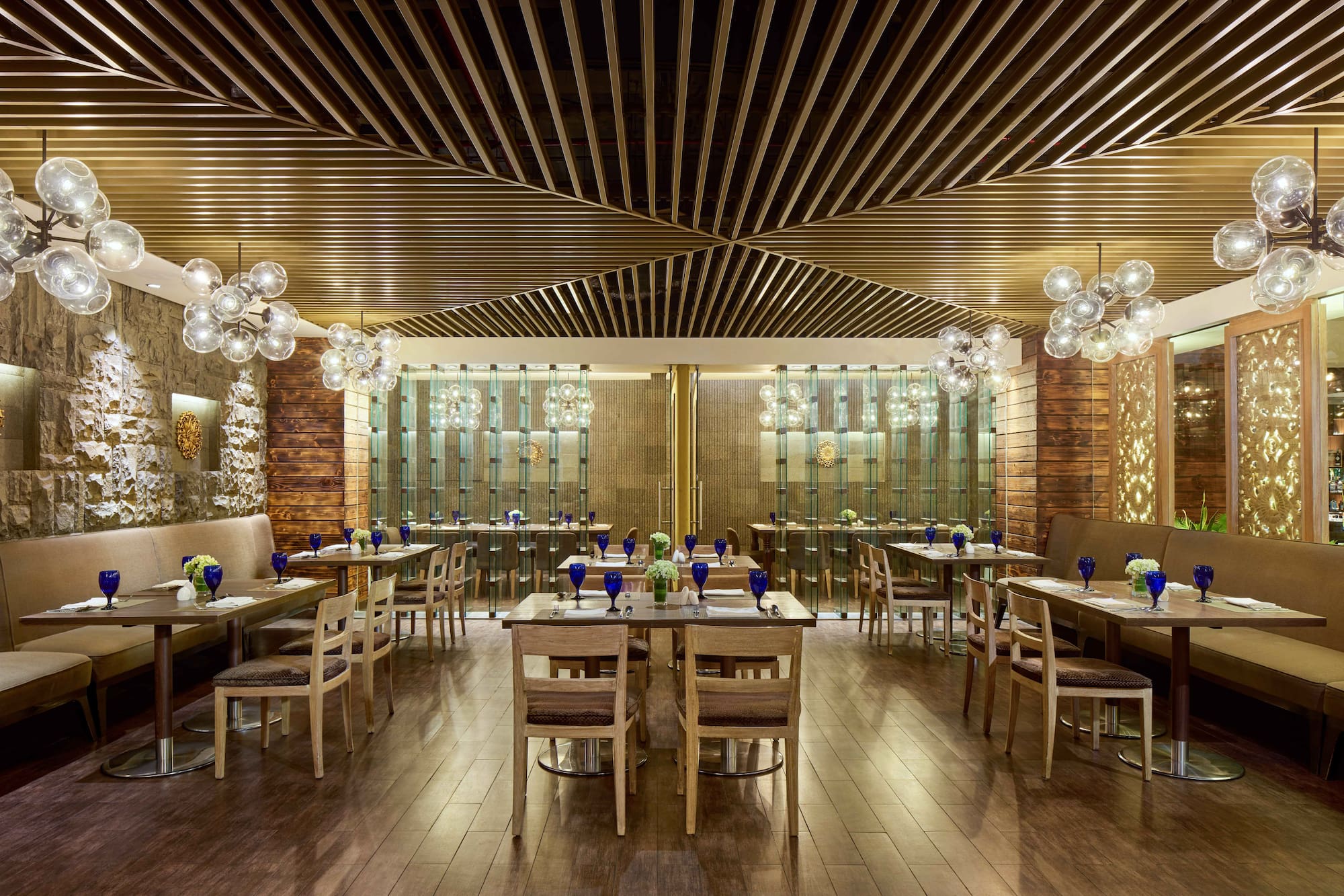 Restaurant interior with wooden tables, banquettes, and modern sphere chandeliers.