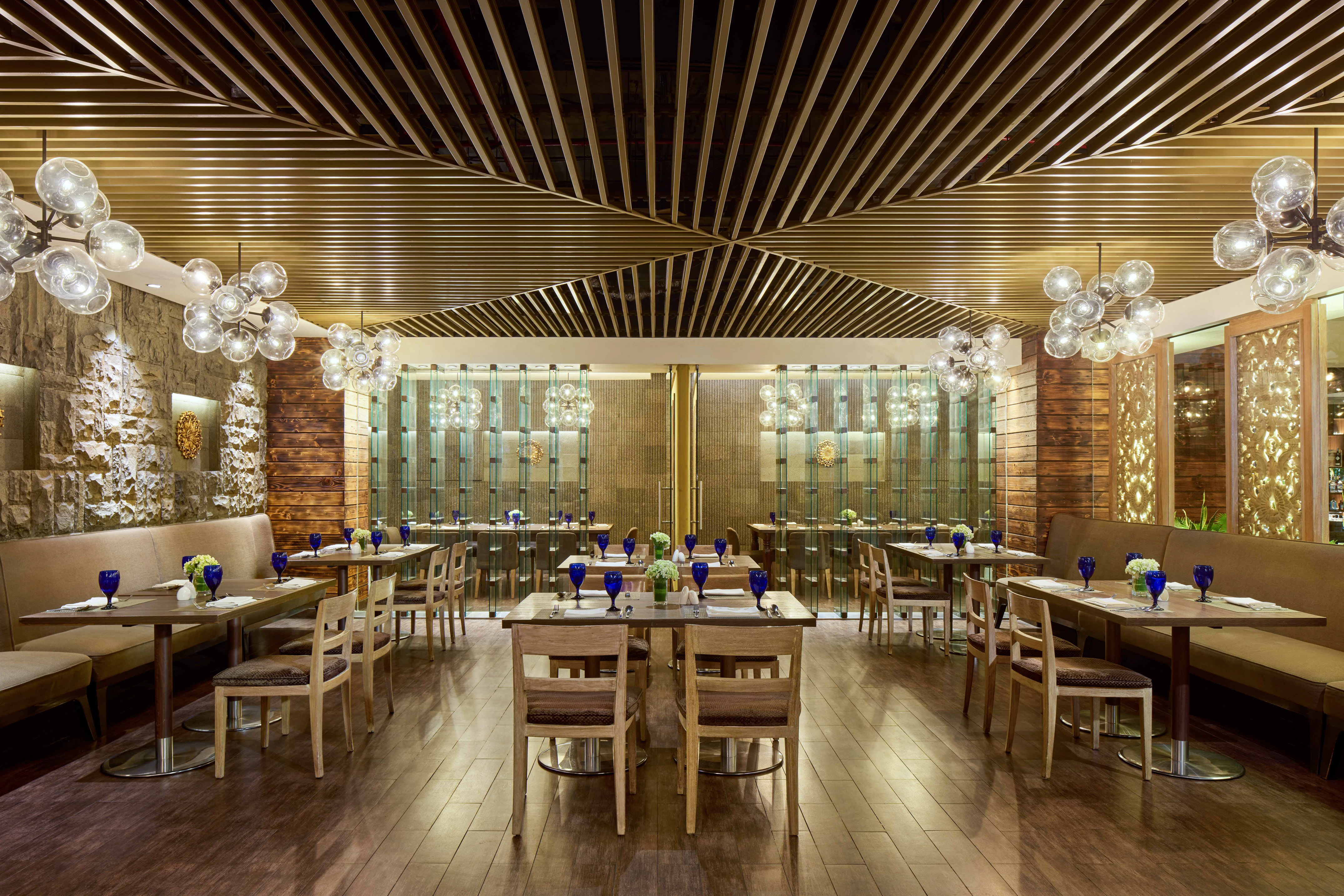 Restaurant interior with wooden tables, banquettes, and modern sphere chandeliers.