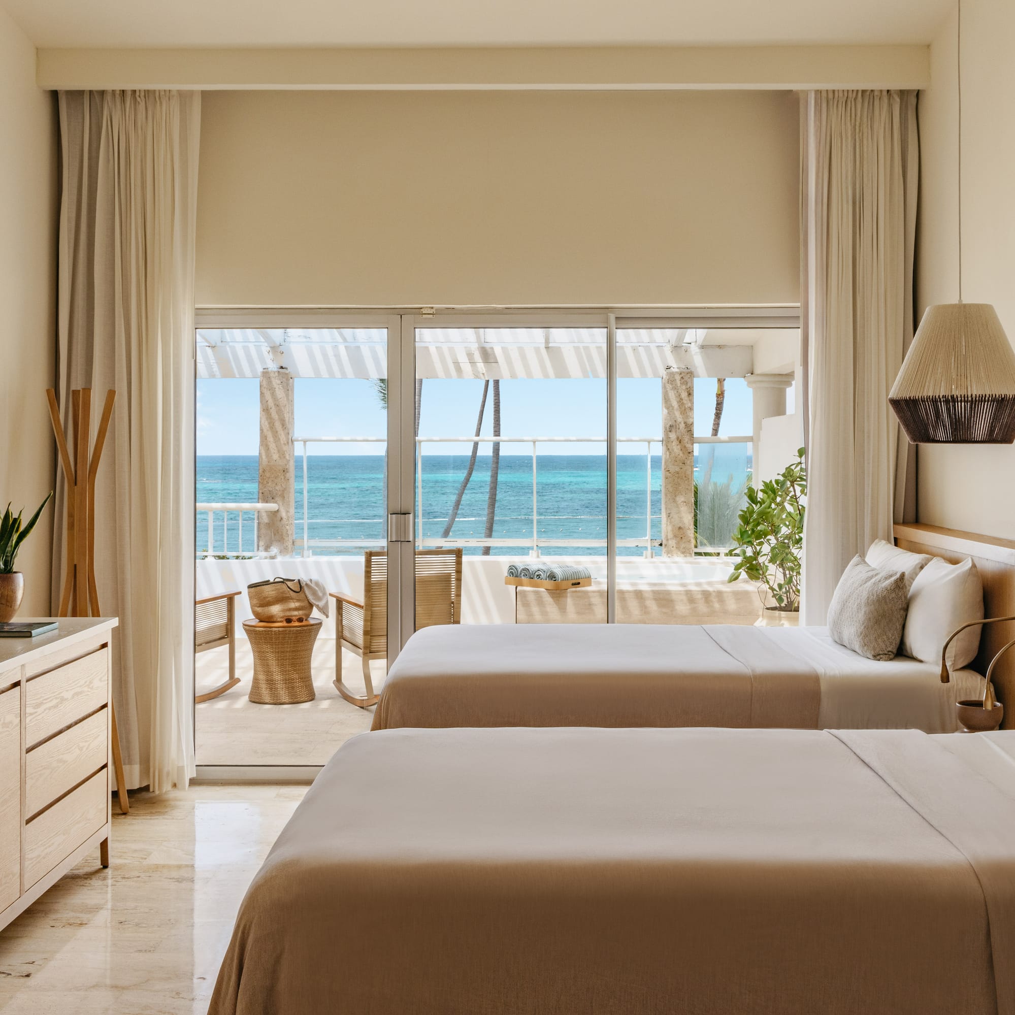 Modern hotel room with two beds, neutral decor, and ocean view balcony.