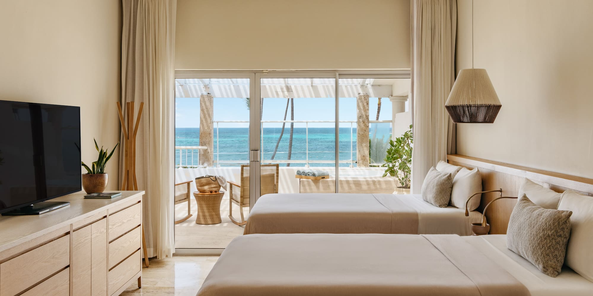 Modern hotel room with two beds, neutral decor, and ocean view balcony.