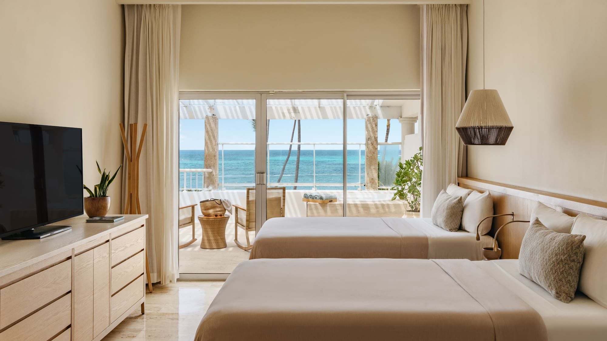 Modern hotel room with two beds, neutral decor, and ocean view balcony.