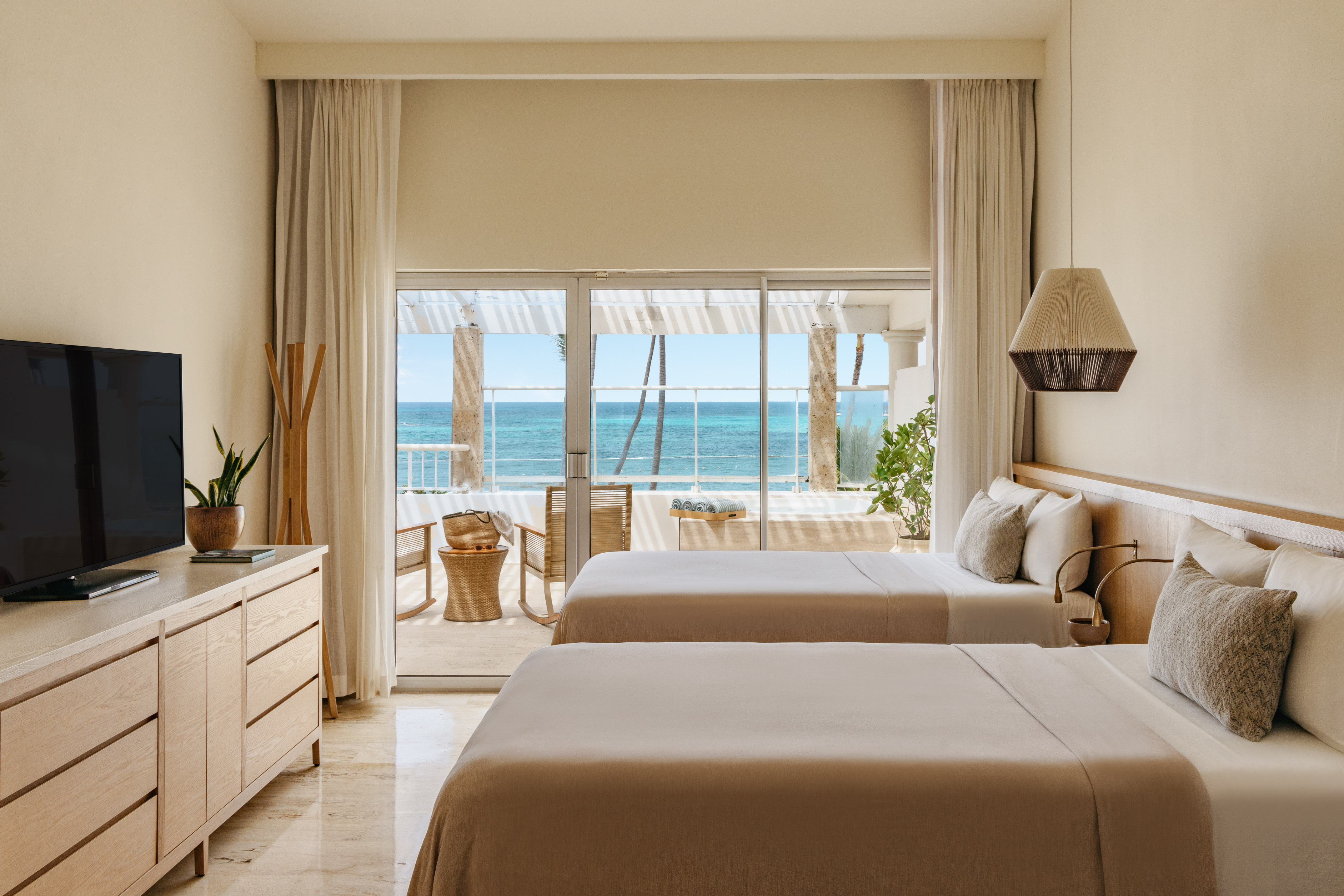 Modern hotel room with two beds, neutral decor, and ocean view balcony.