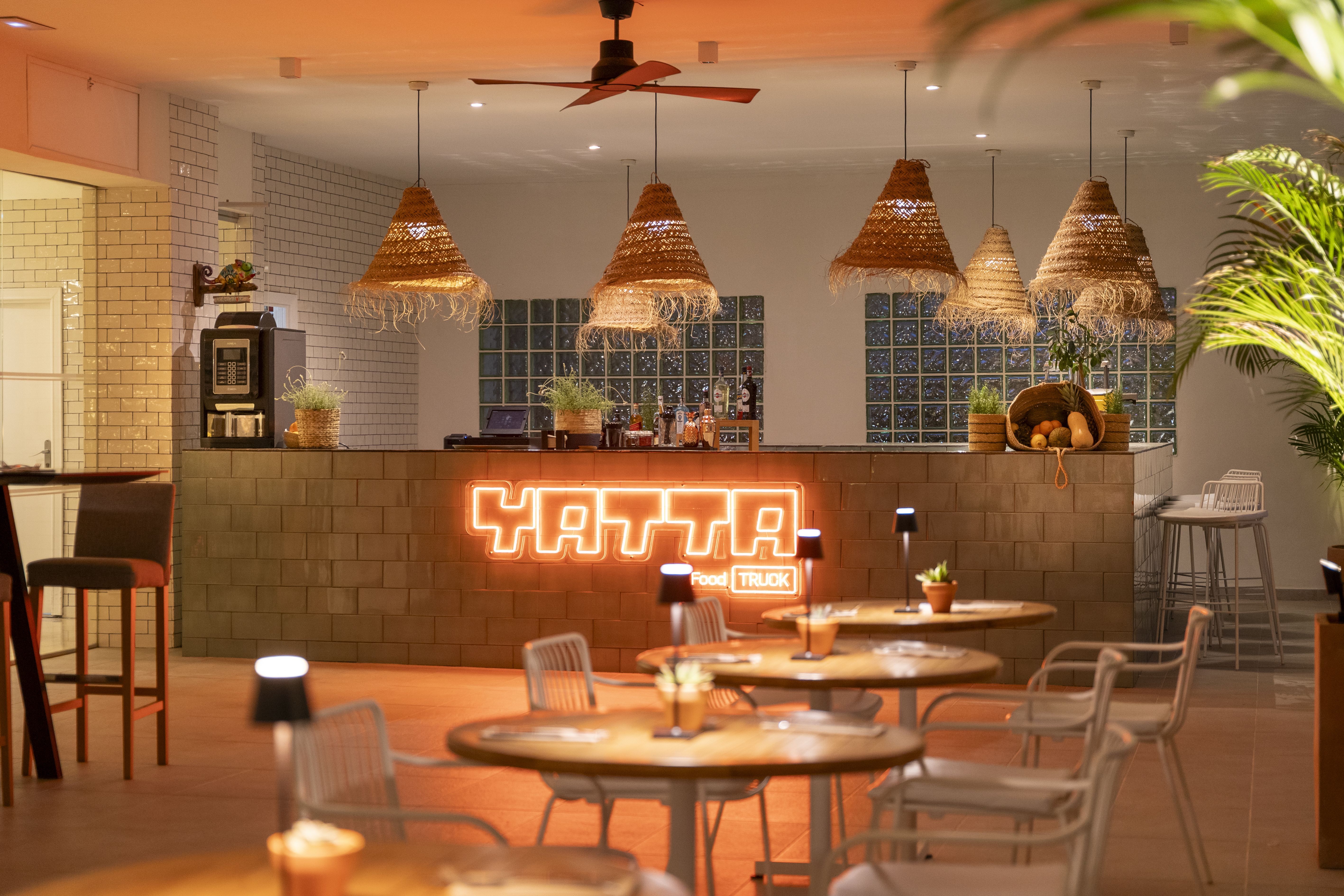 Yatta Food Truck bar interior with neon sign, wicker lights, and dining tables.