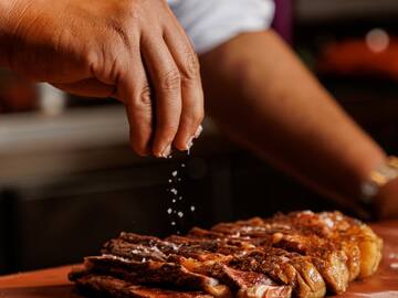 a person sprinkling salt on a piece of meat