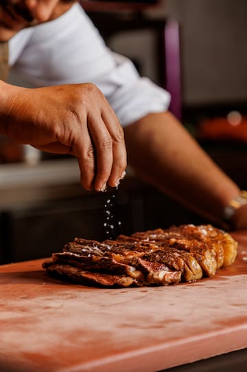 a person sprinkling salt on a piece of meat