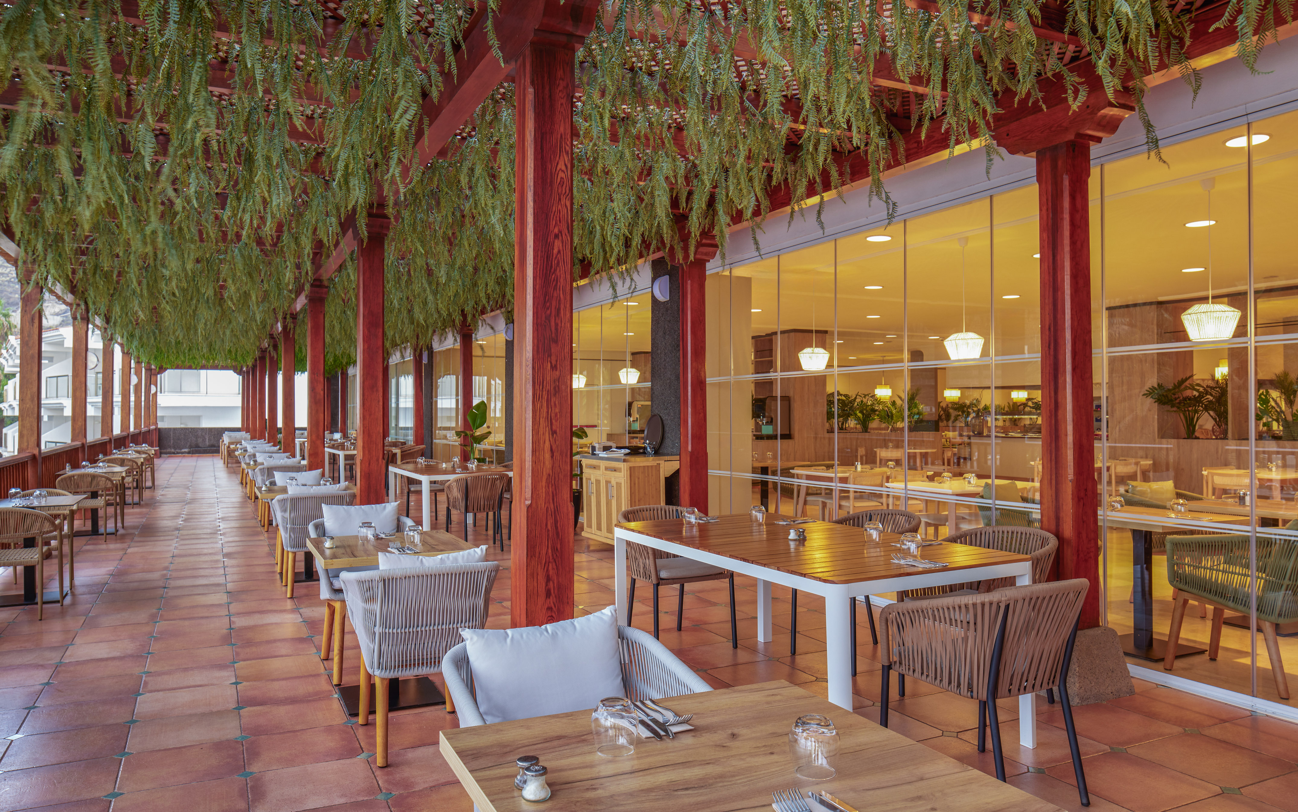 Dining terrace with a wooden pergola, hanging green foliage, and set tables.