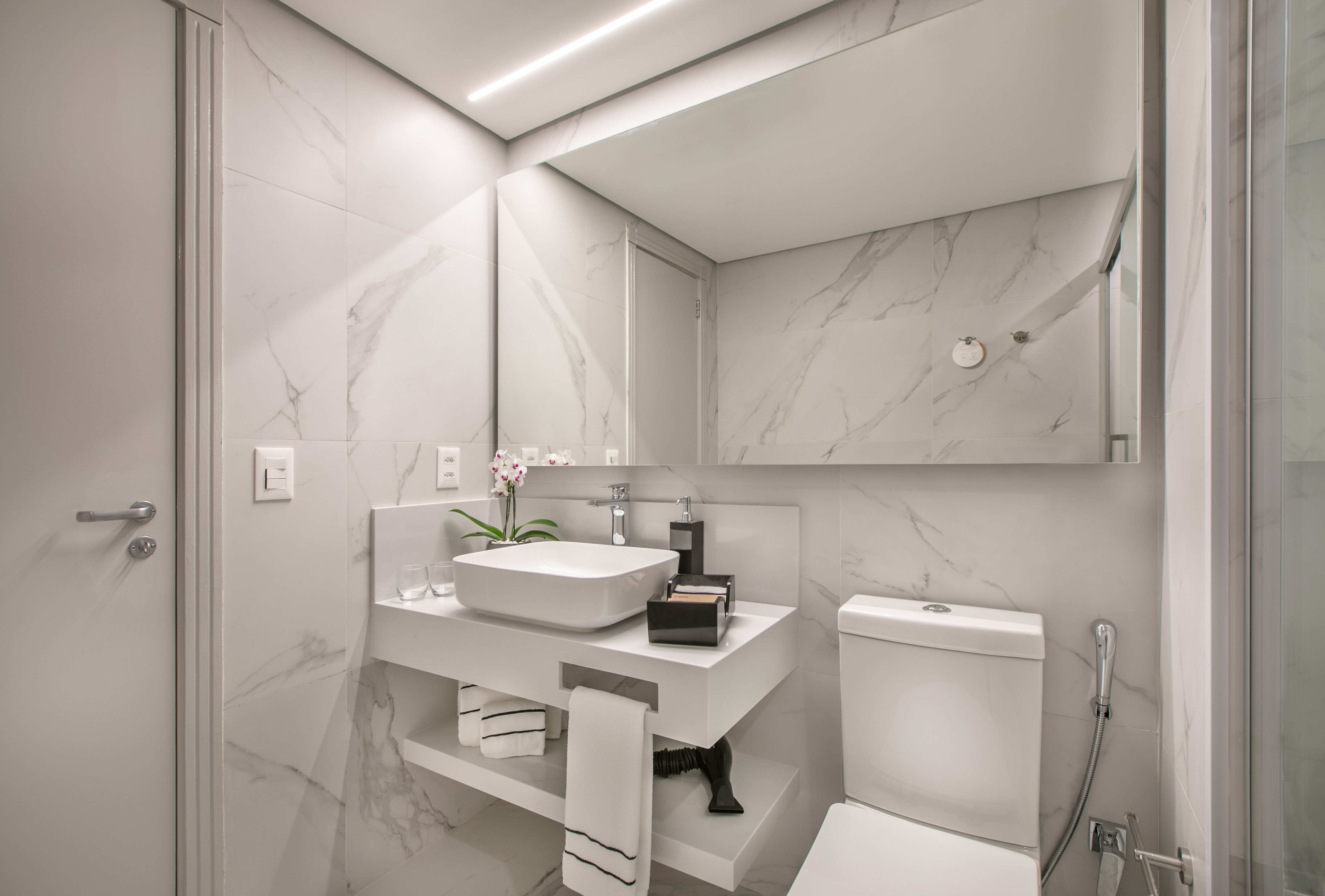 Modern white bathroom with marble tiles, floating vanity, vessel sink, and mirror.