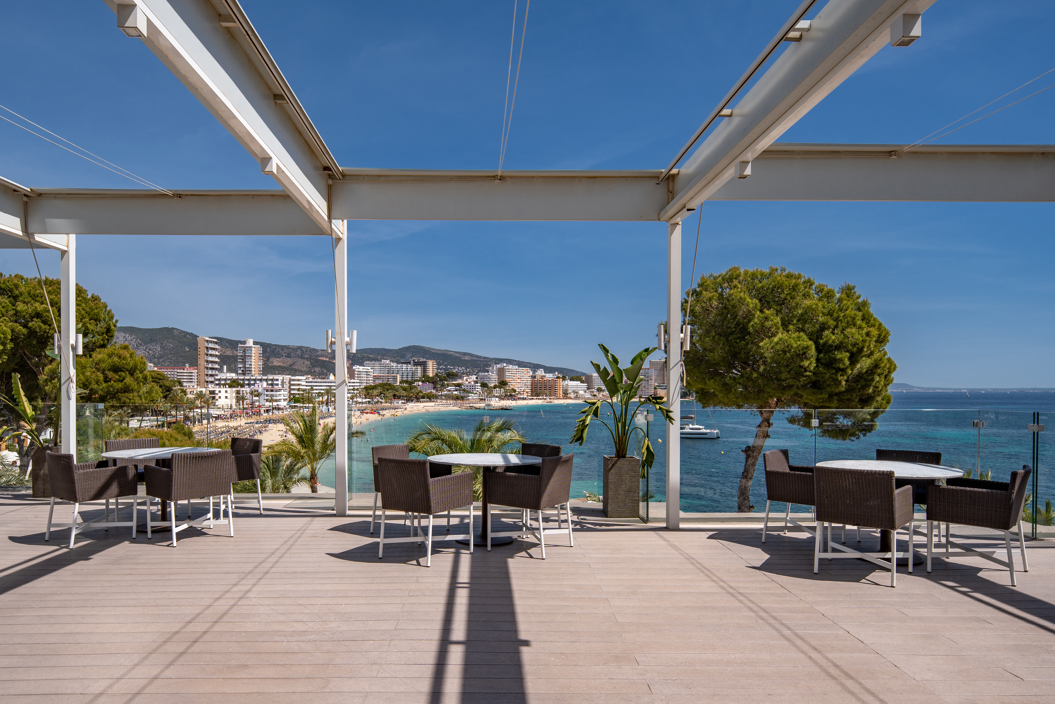Sunny resort terrace with sea view, sandy beach, and coastal town.
