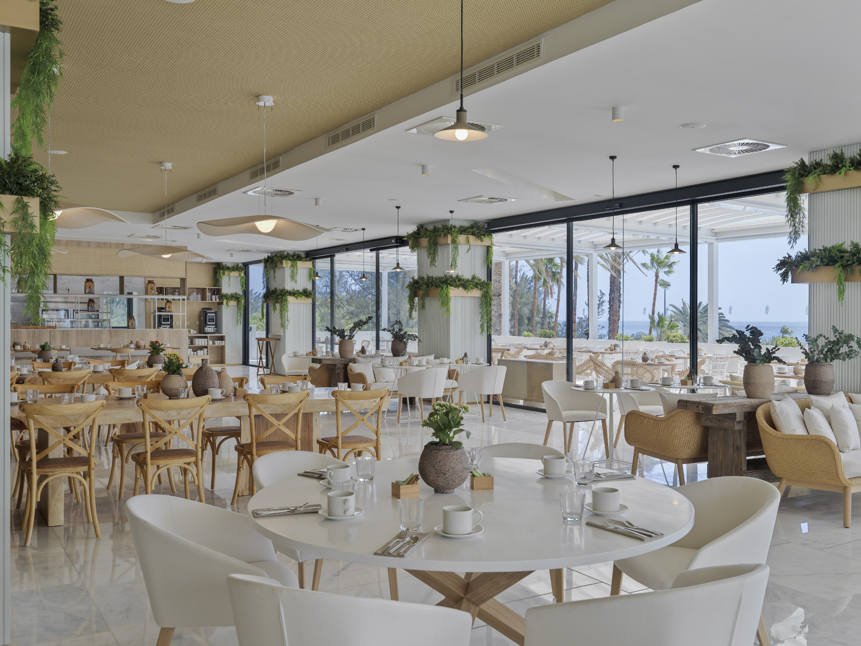 Coastal hotel restaurant interior with ocean view, modern decor, and lush plants.