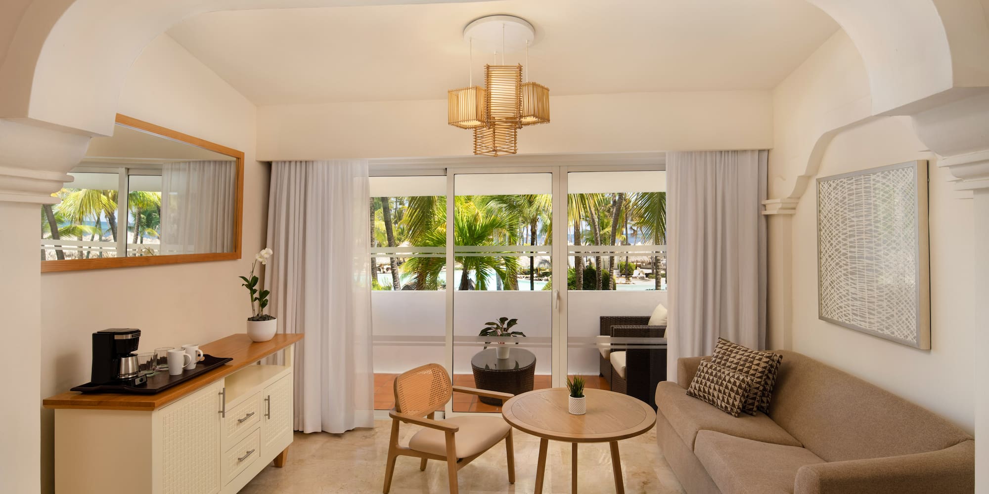 Hotel suite living room with sofa, balcony, and tropical palm tree view.