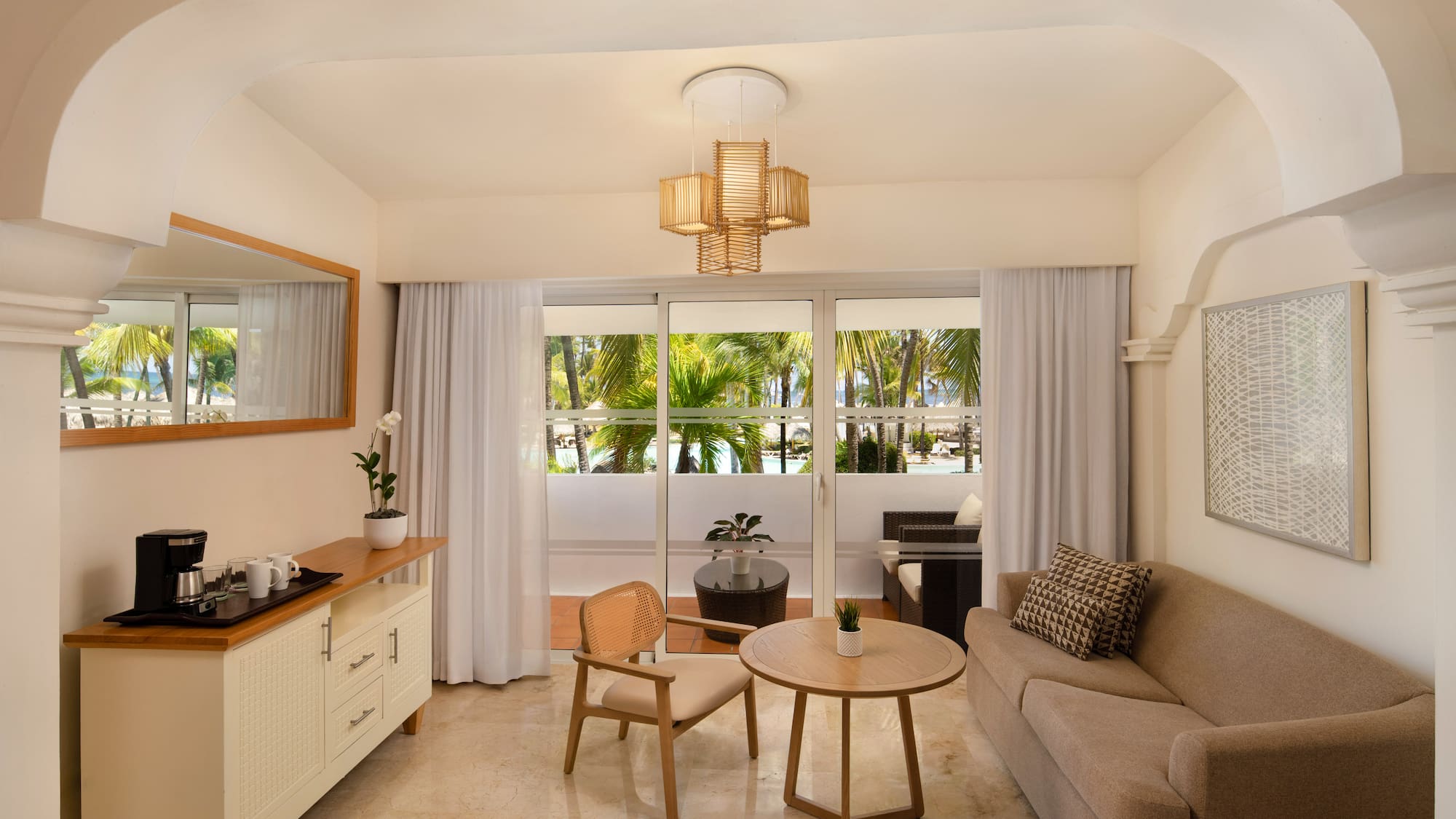 Hotel suite living room with sofa, balcony, and tropical palm tree view.