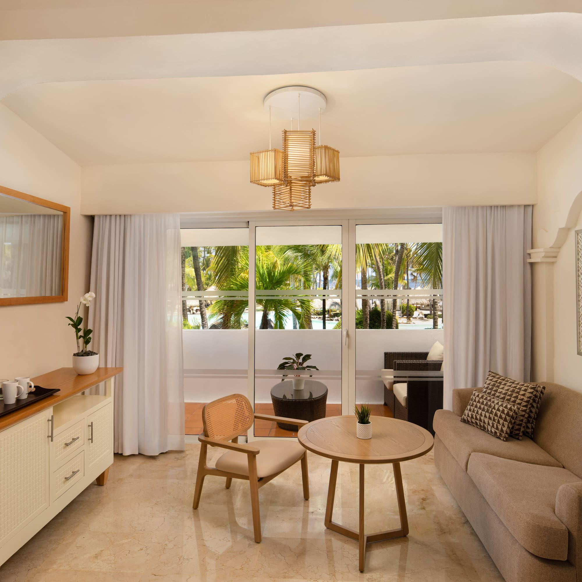 Hotel suite living room with sofa, balcony, and tropical palm tree view.