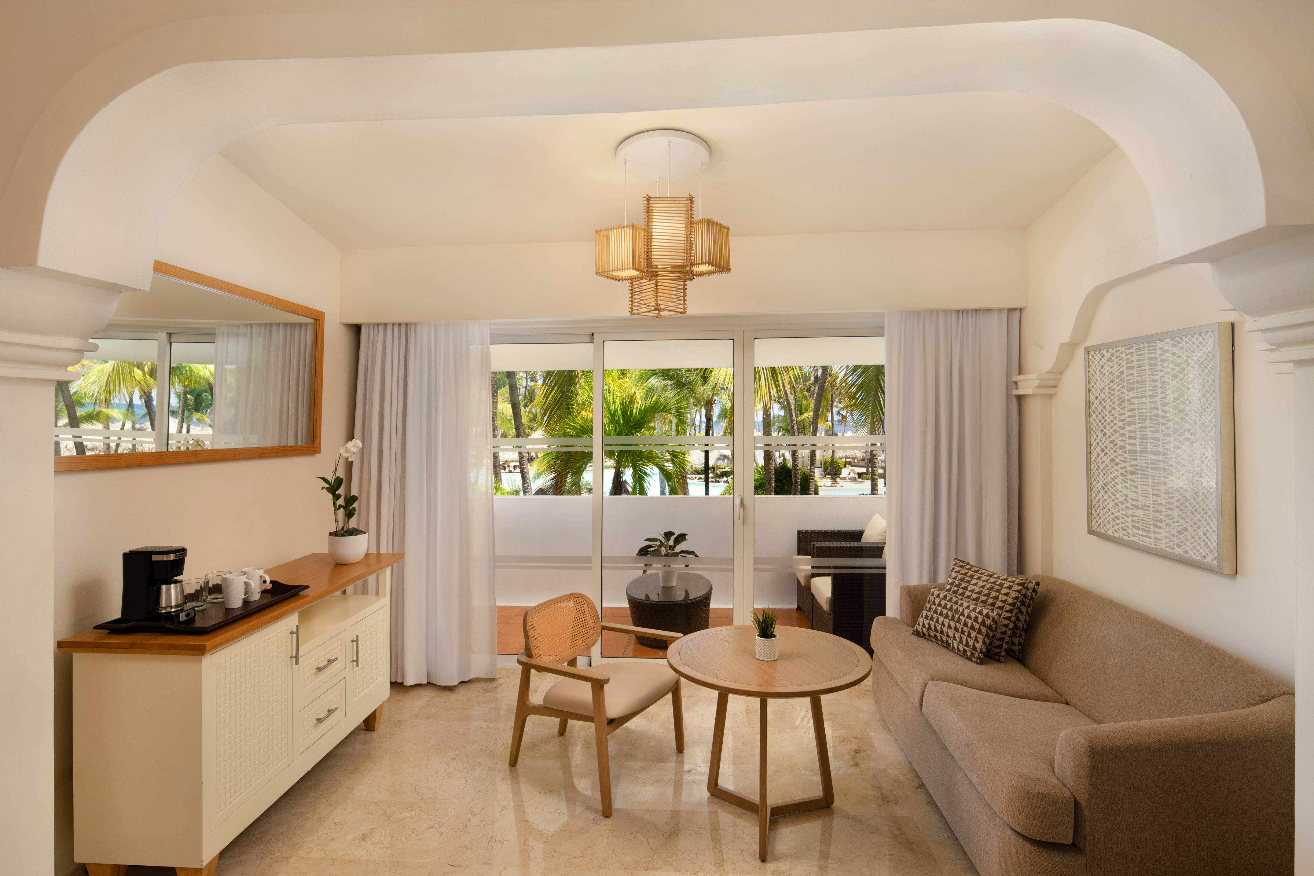 Hotel suite living room with sofa, balcony, and tropical palm tree view.