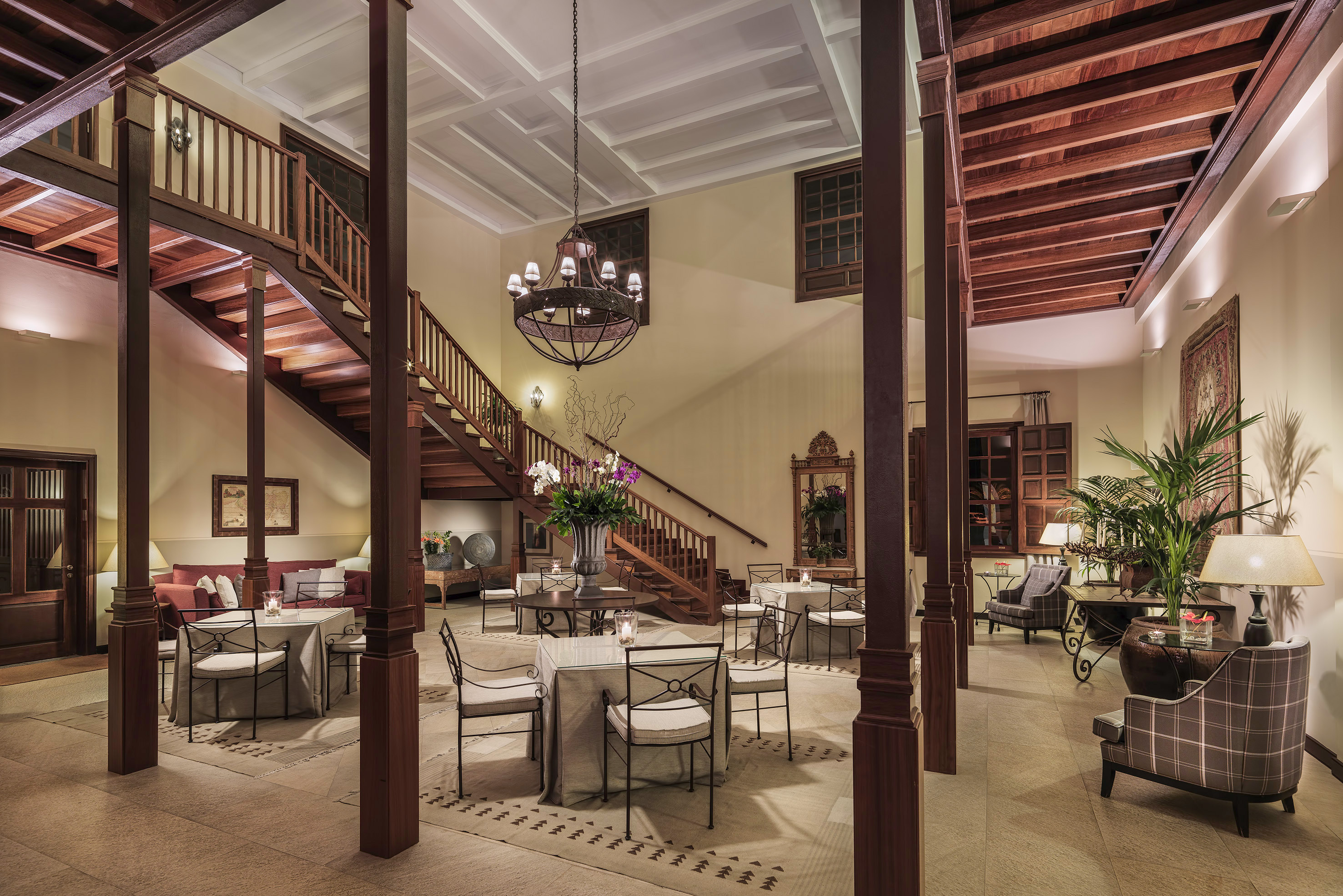 Elegant hotel lobby with grand wooden staircase, chandelier, and dining tables.