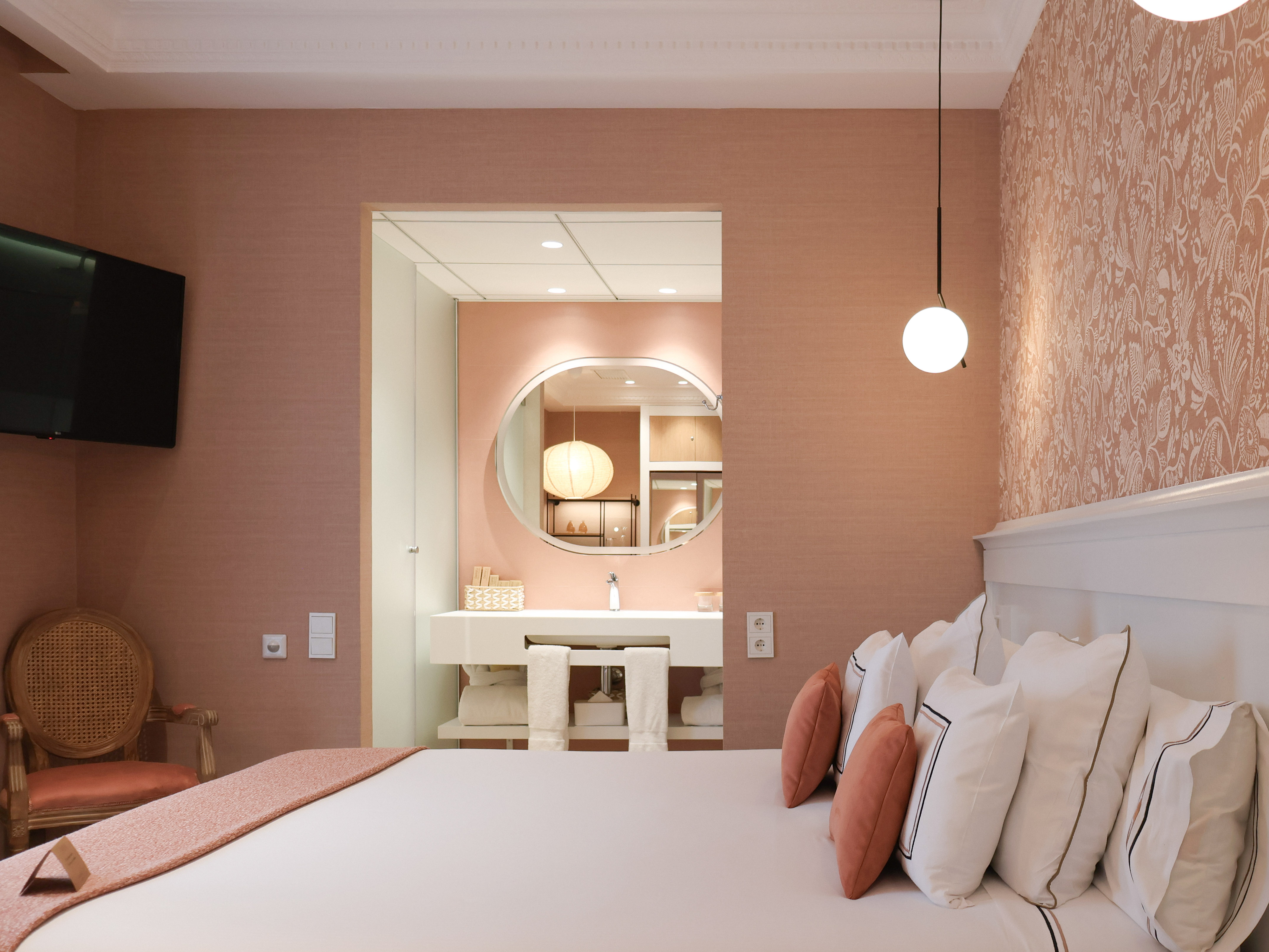 Peach and white hotel bedroom with bed, vanity area, TV, and patterned wall.