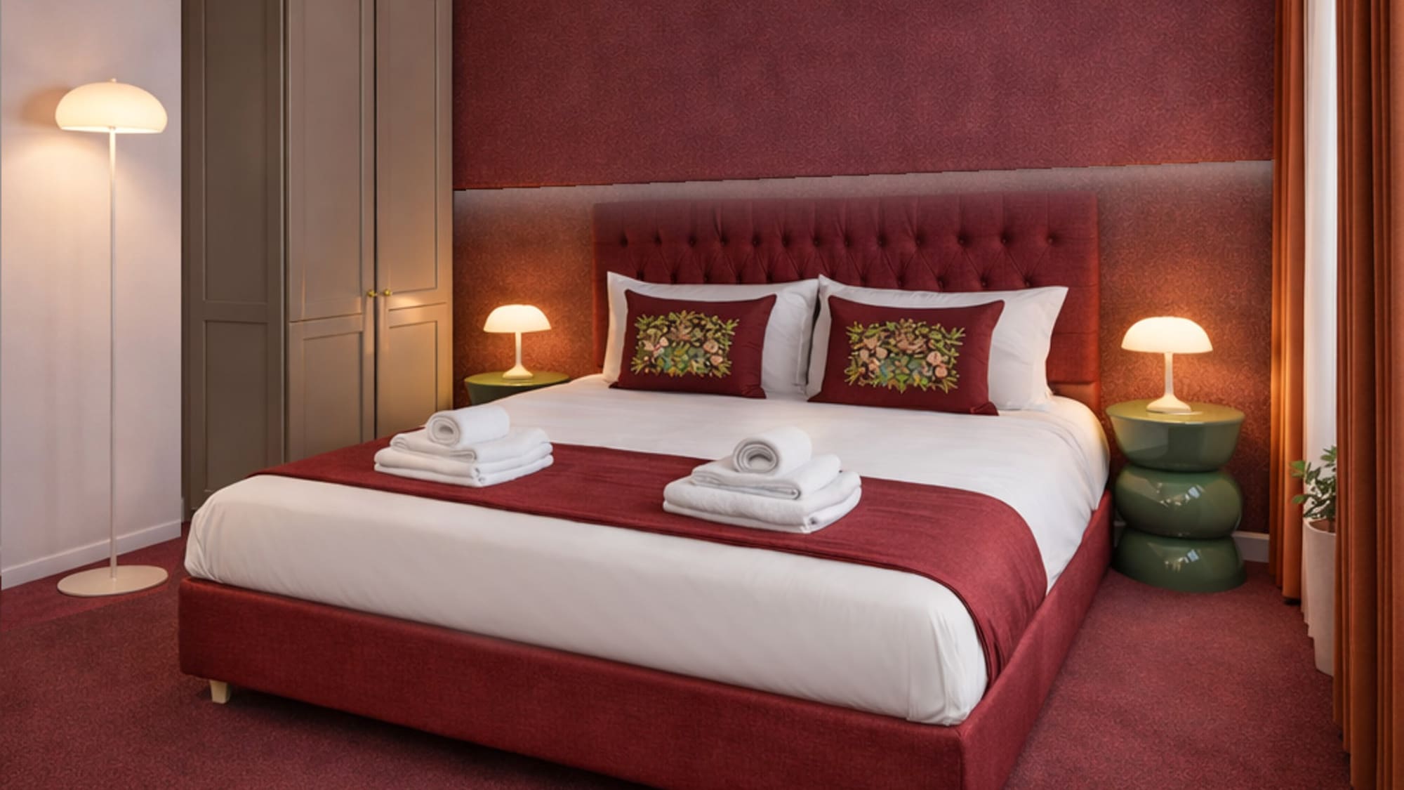 Red bedroom with plush bed, embroidered pillows, and modern lamps.