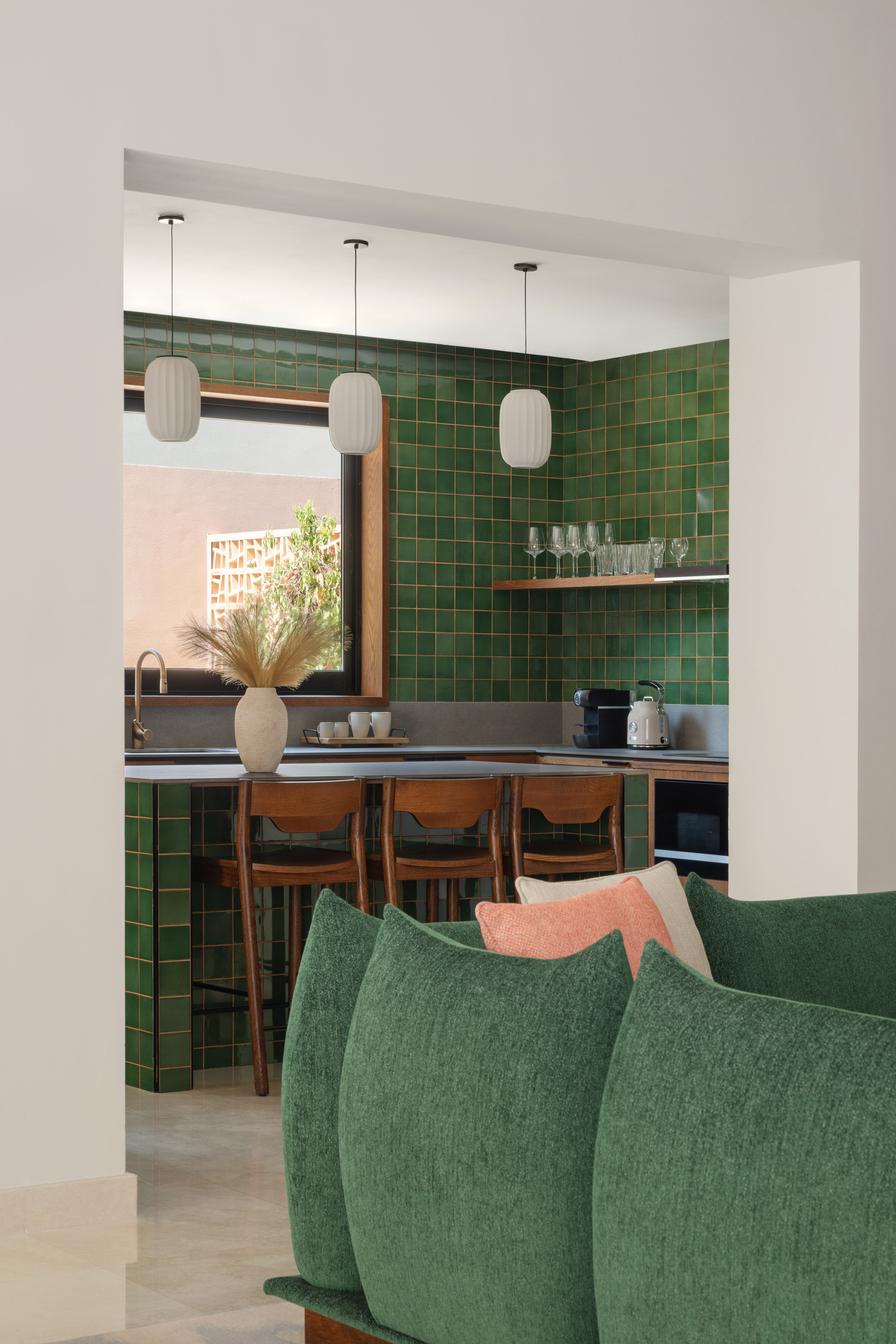 Contemporary kitchen featuring green tiles, wooden bar stools, and a green sofa.