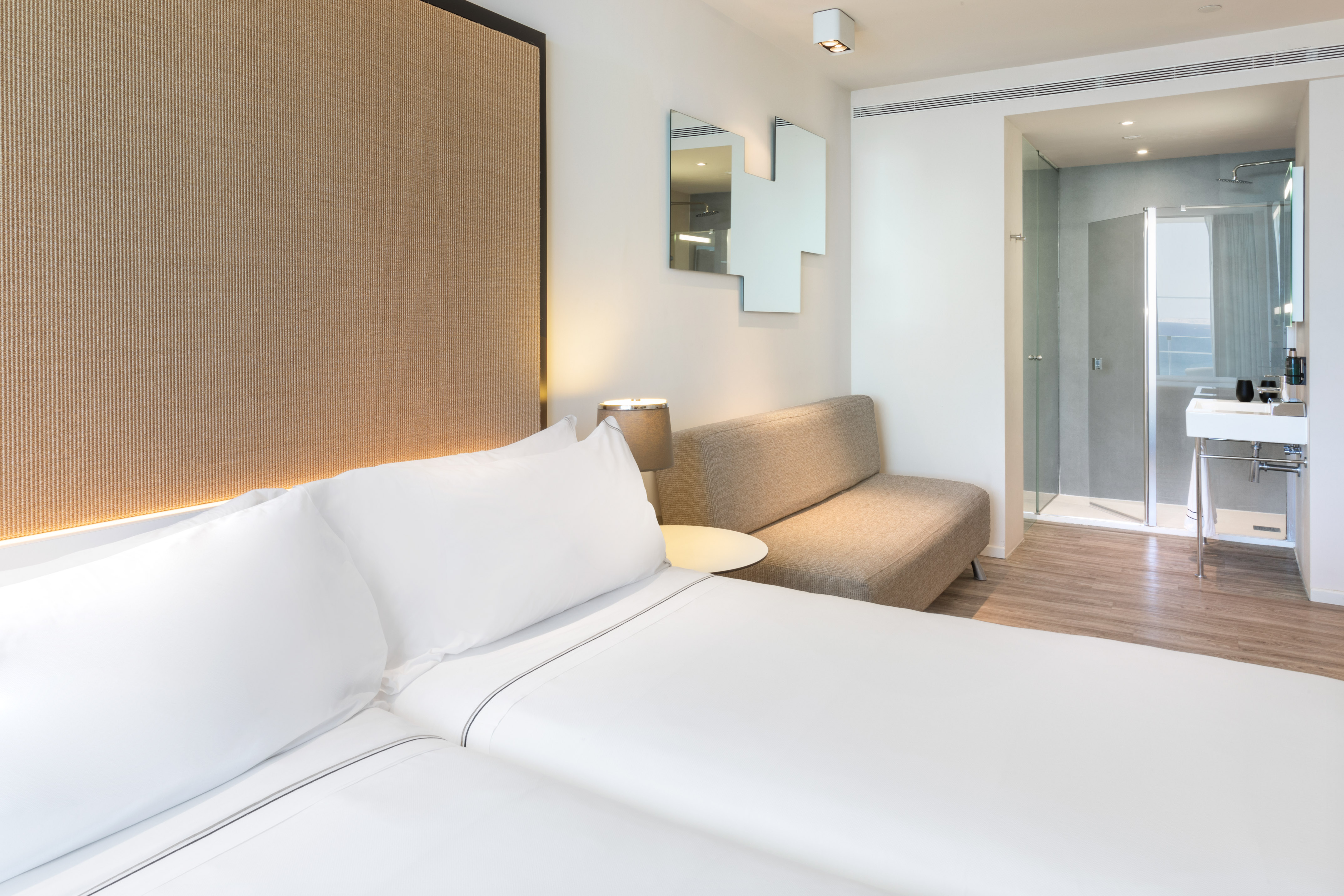Clean, modern hotel room with white bed, sofa, and en-suite shower.