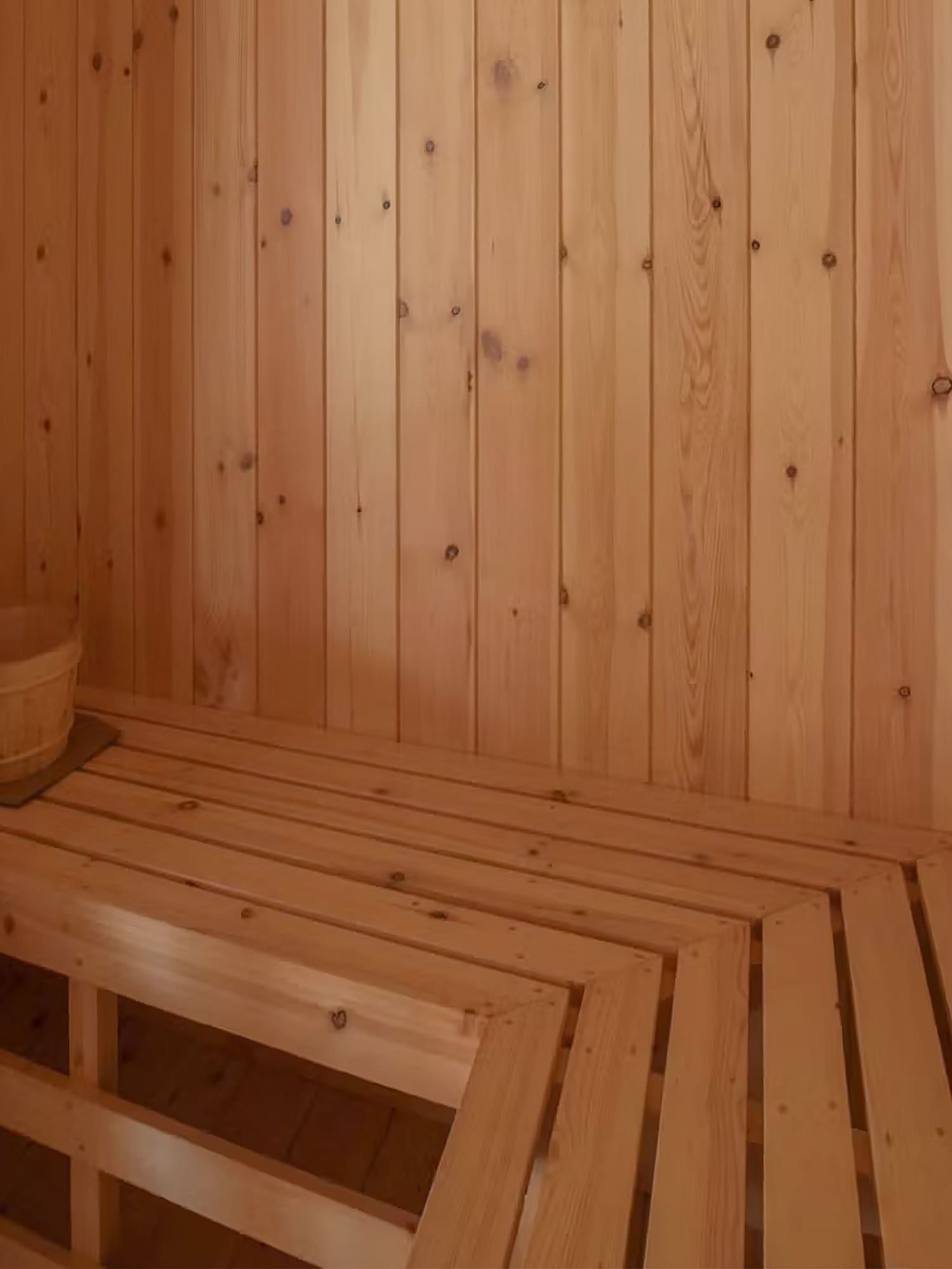 Interior de sauna de madera clara con bancos, estufa y cubo de agua.