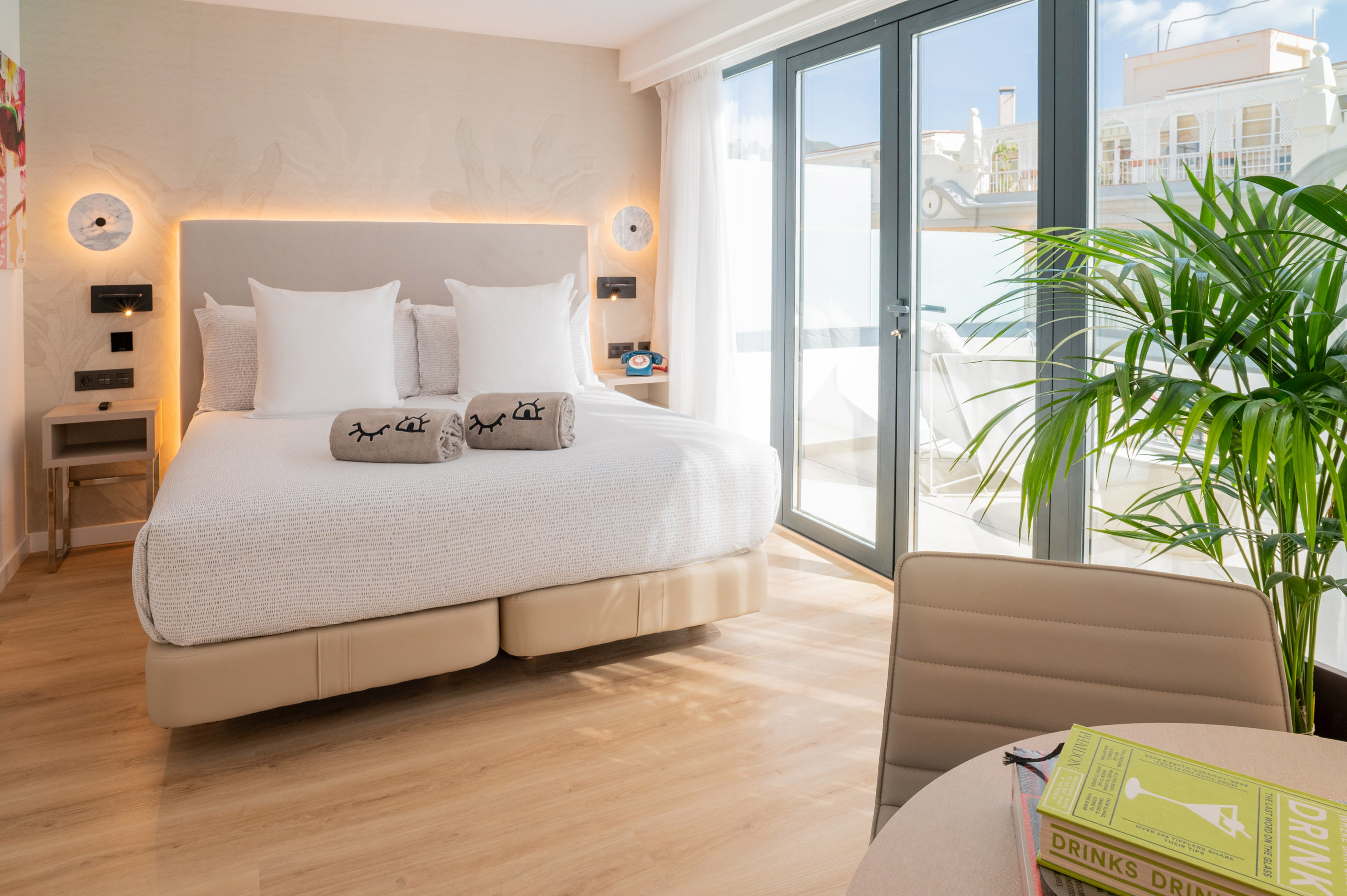 Bright modern hotel room with large bed, balcony, wooden floor, and a plant.