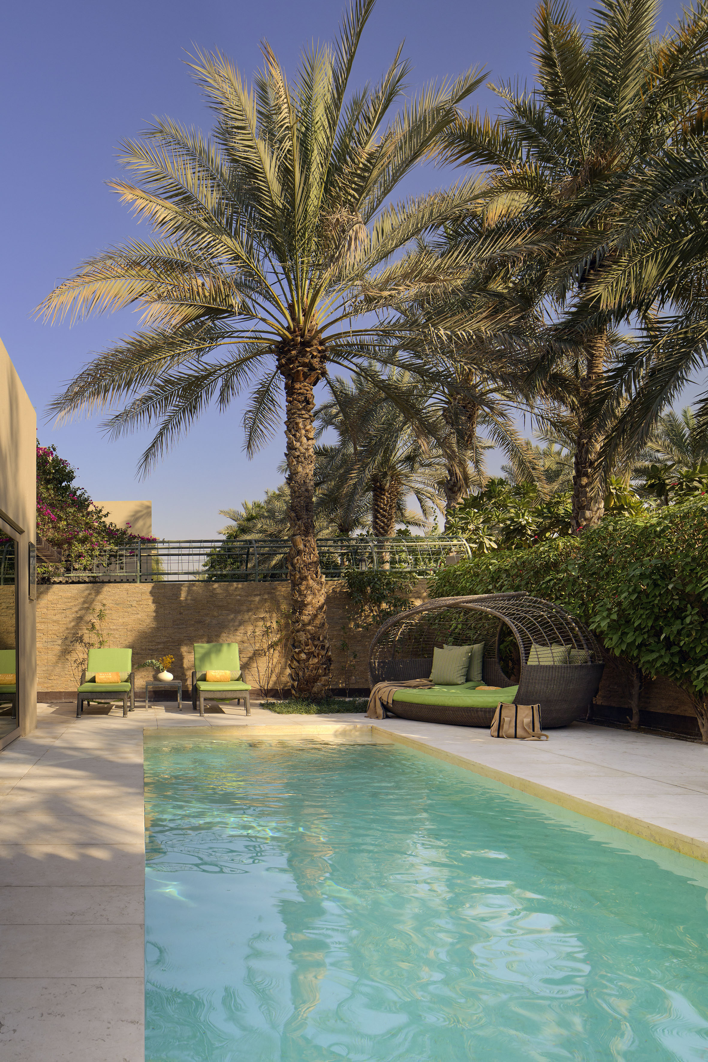 Private villa pool with palm trees, green lounge chairs, and wicker daybed.