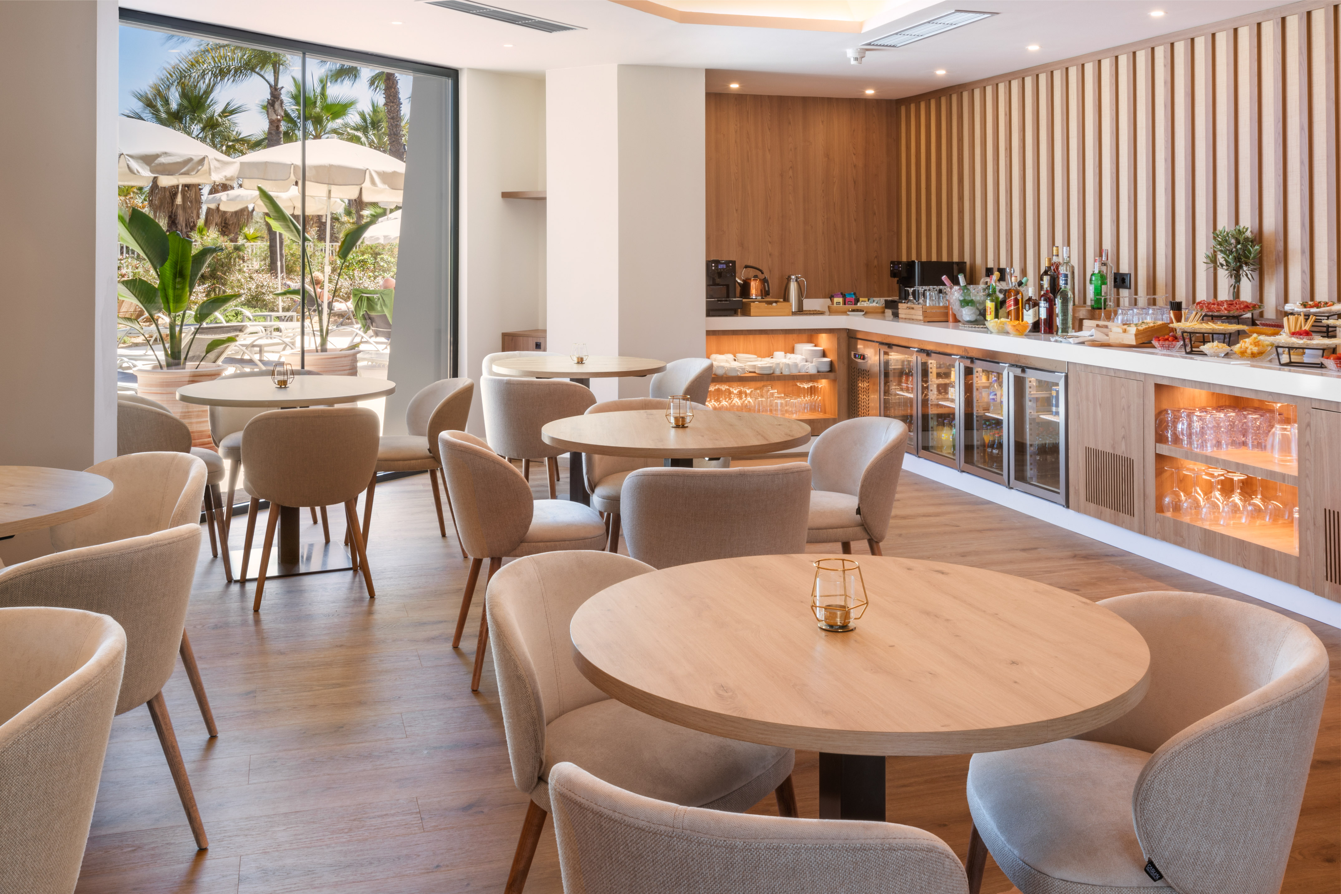 Contemporary hotel lounge with buffet, seating, and lush outdoor patio view.