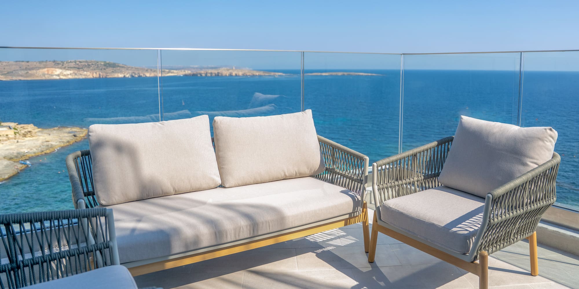 Modern woven outdoor sofa and chairs on balcony with blue sea view.