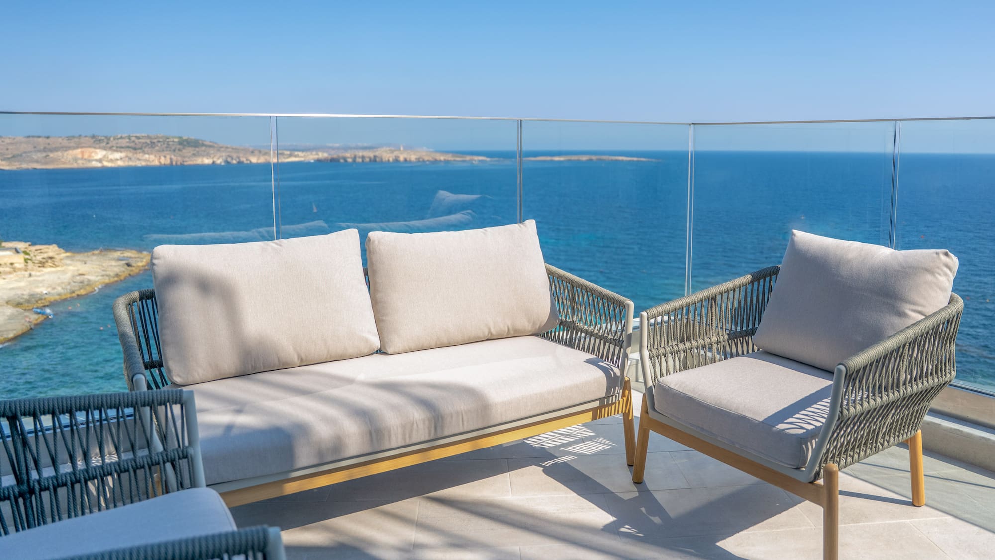 Modern woven outdoor sofa and chairs on balcony with blue sea view.