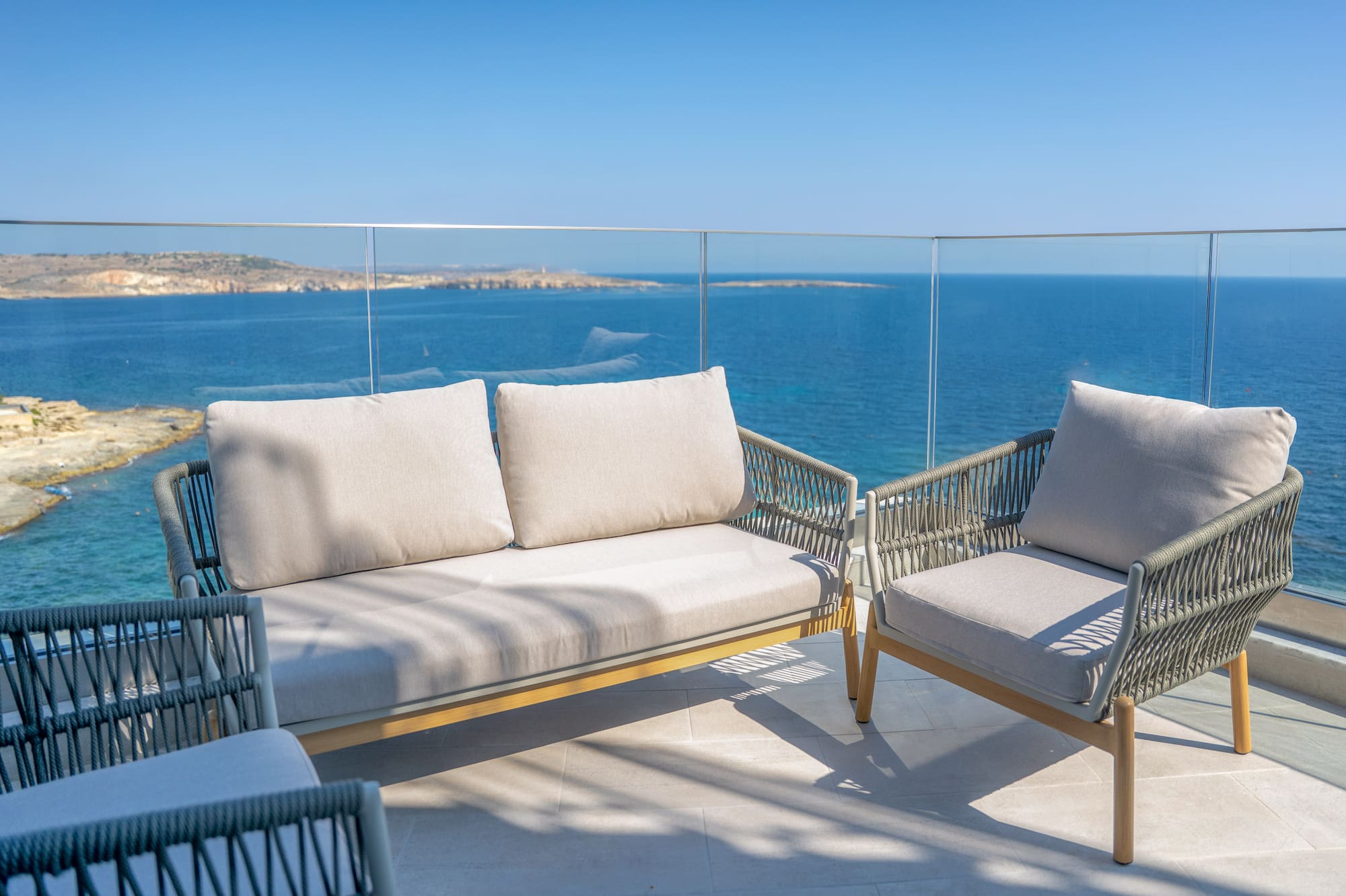 Modern woven outdoor sofa and chairs on balcony with blue sea view.