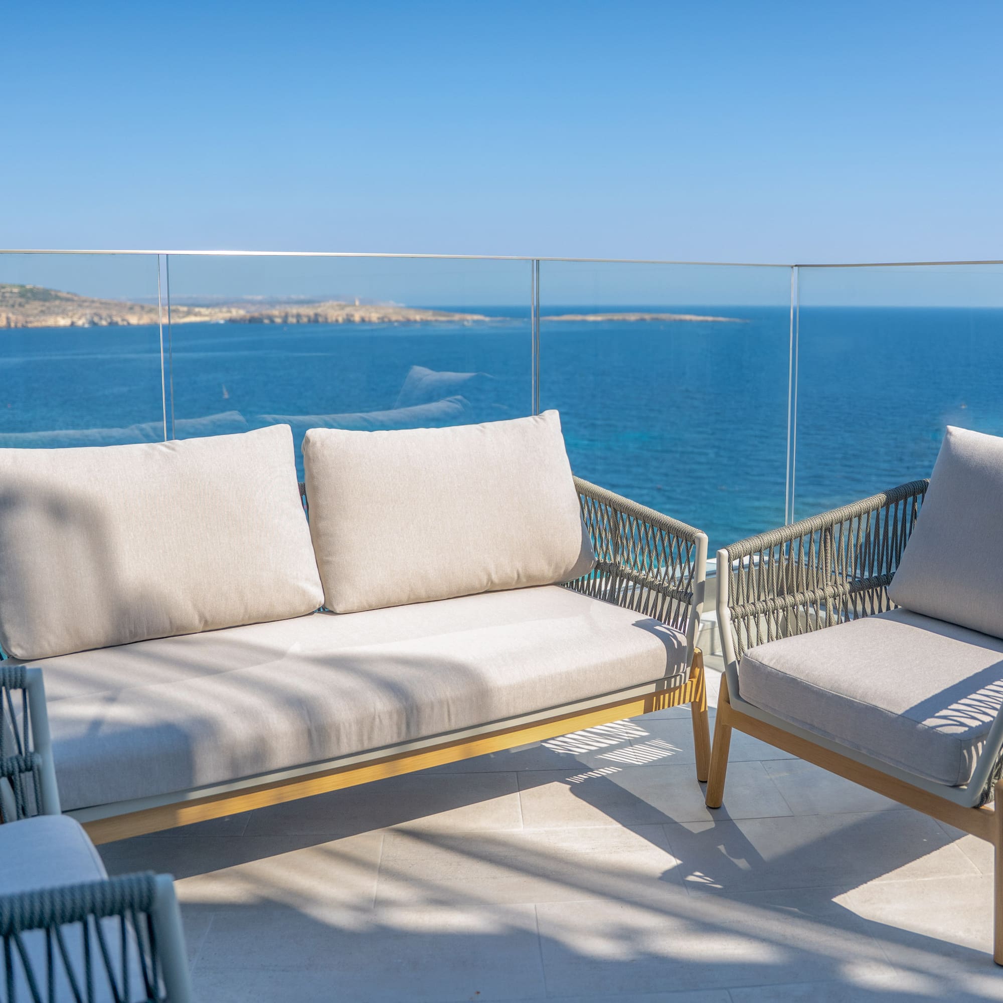 Modern woven outdoor sofa and chairs on balcony with blue sea view.