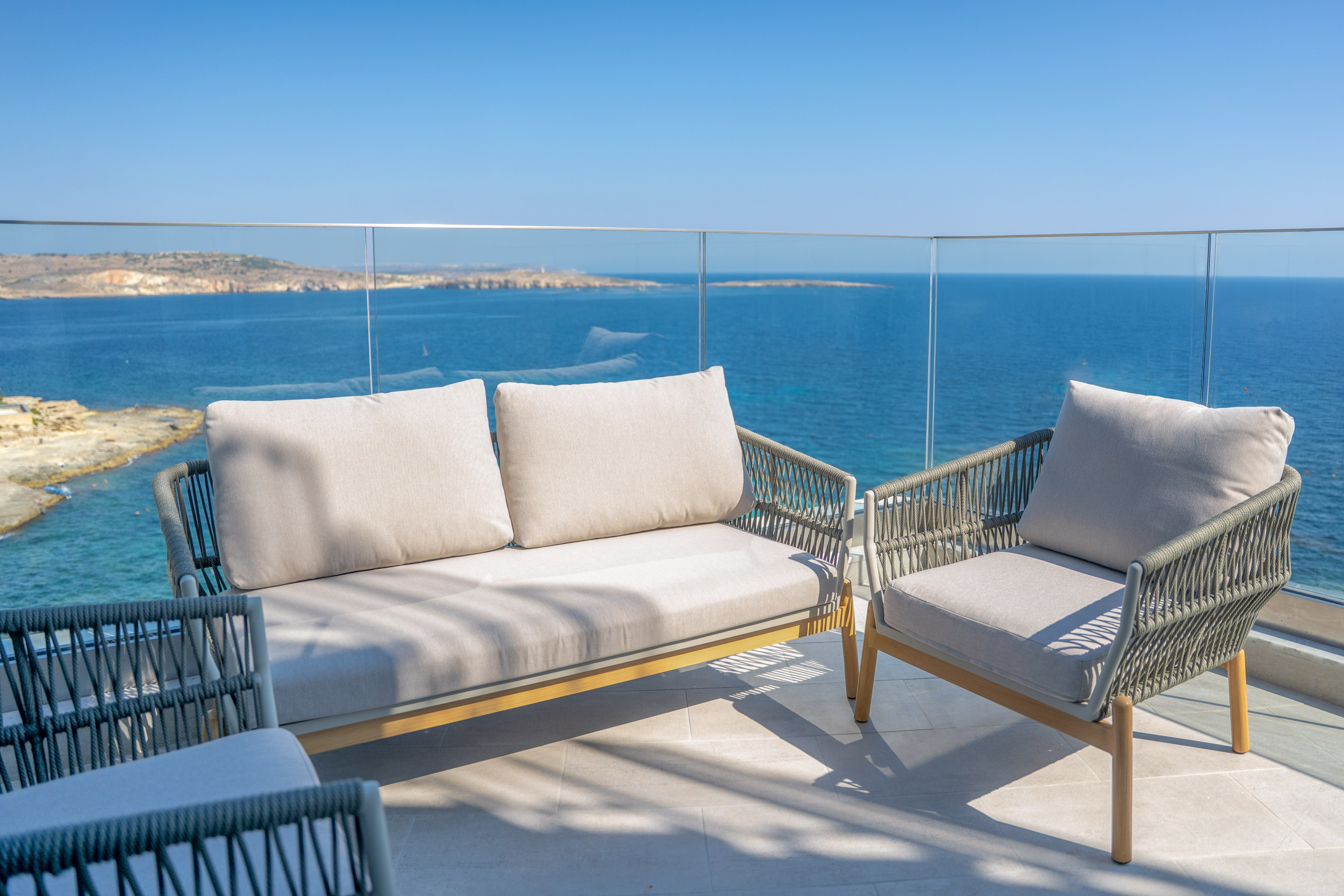 Modern woven outdoor sofa and chairs on balcony with blue sea view.