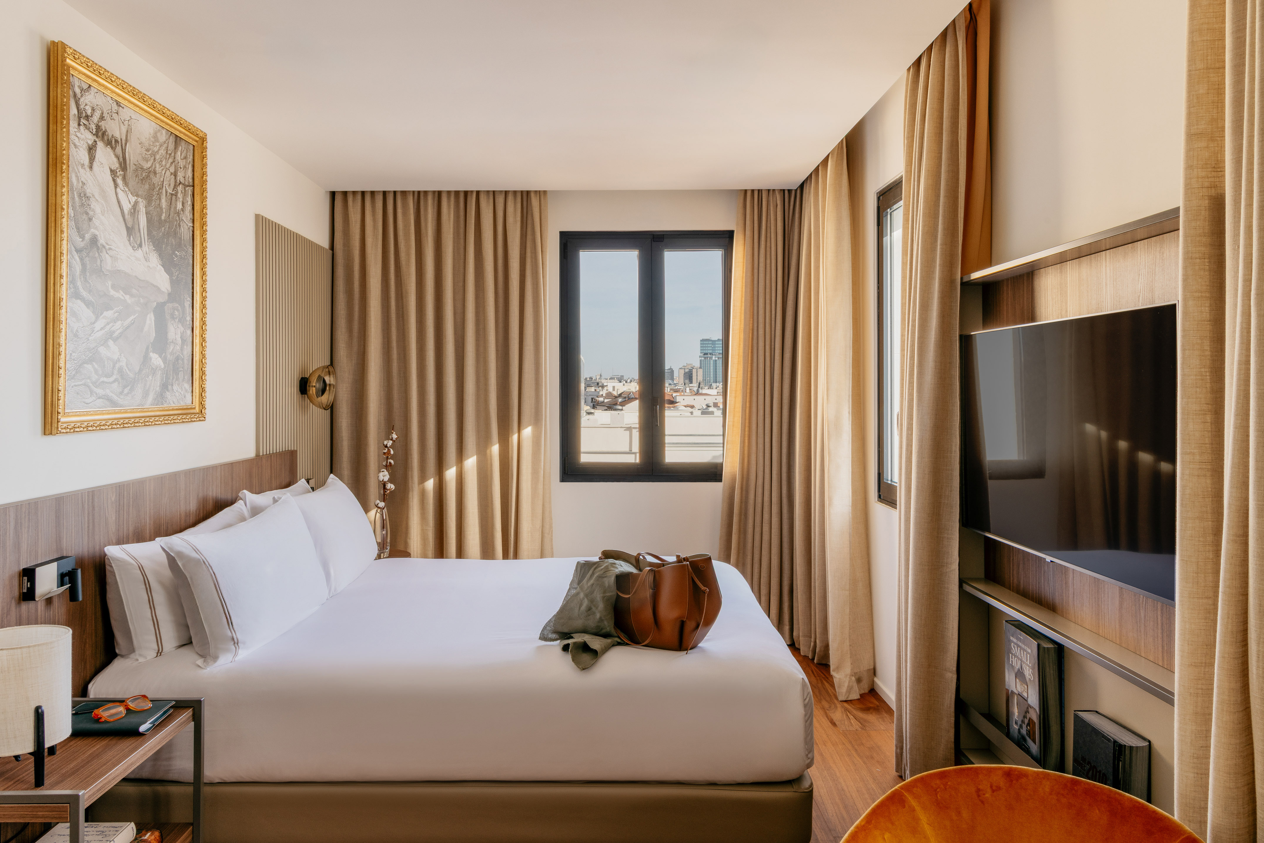 Modern hotel bedroom with large white bed, city view, and hardwood floor.