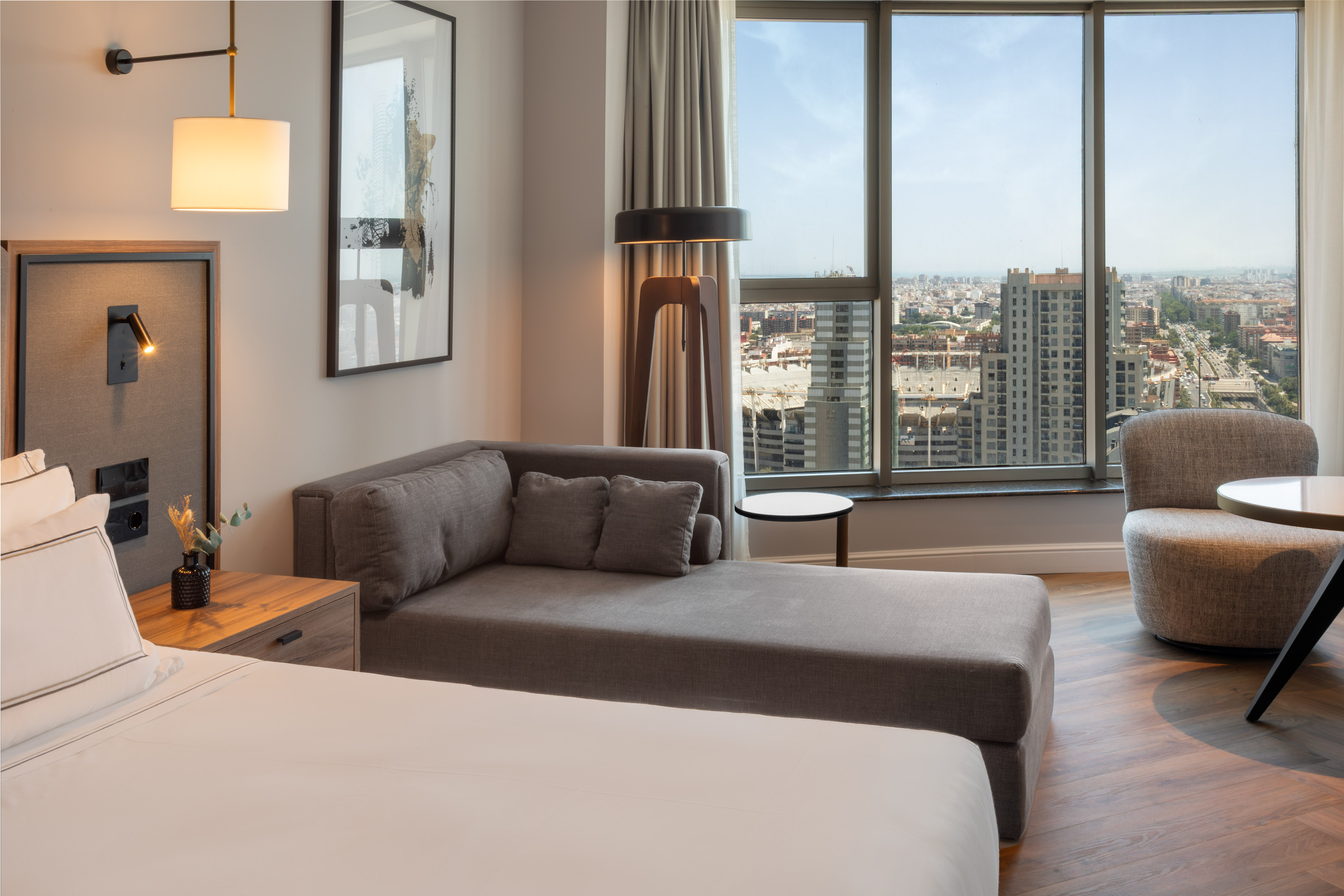 Suite de hotel moderna con vista a la ciudad, cama y chaise longue.