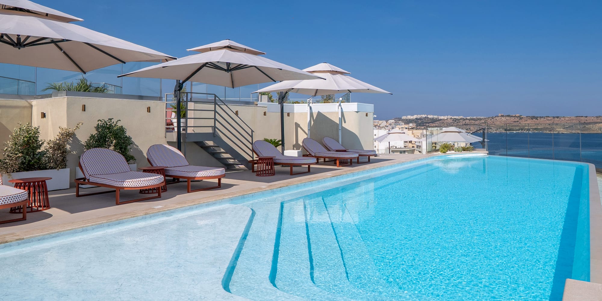 Rooftop infinity pool with lounge chairs, umbrellas, and expansive ocean view.