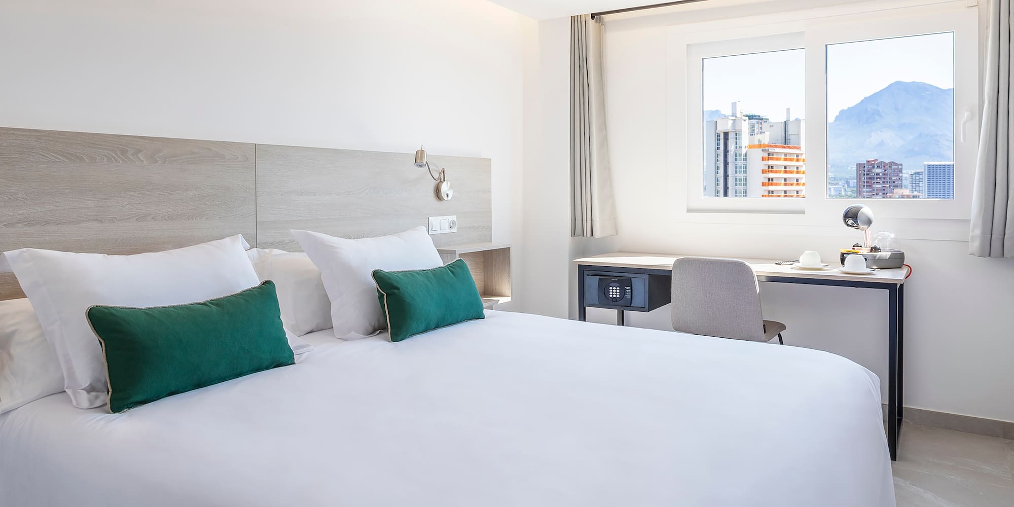 a bed with white sheets and green pillows in a room with a window