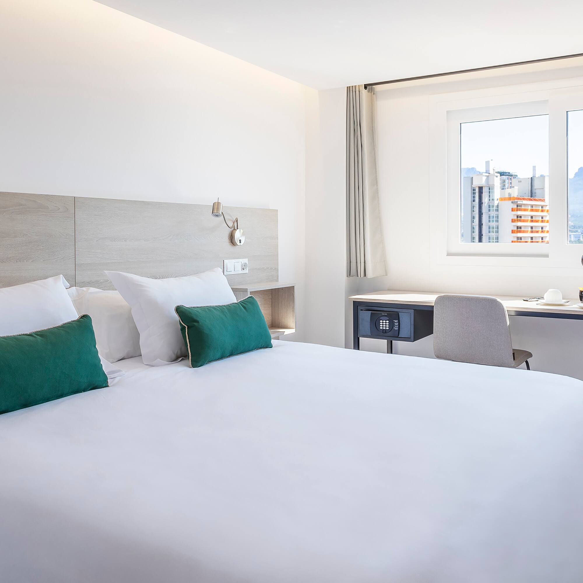 a bed with white sheets and green pillows in a room with a window