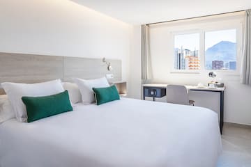 a bed with white sheets and green pillows in a room with a window