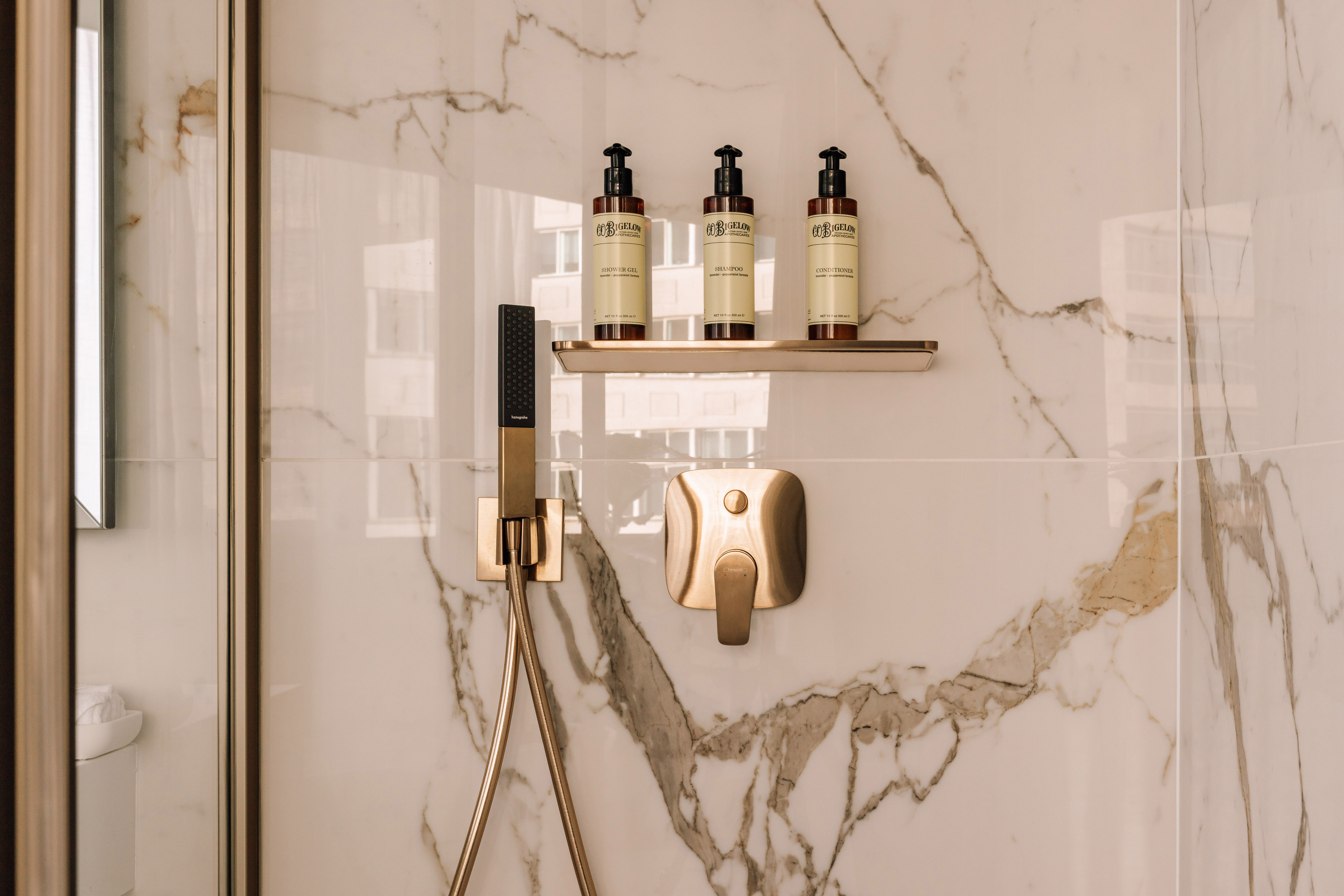 Luxury shower with white marble walls, gold fixtures, and hotel amenities.