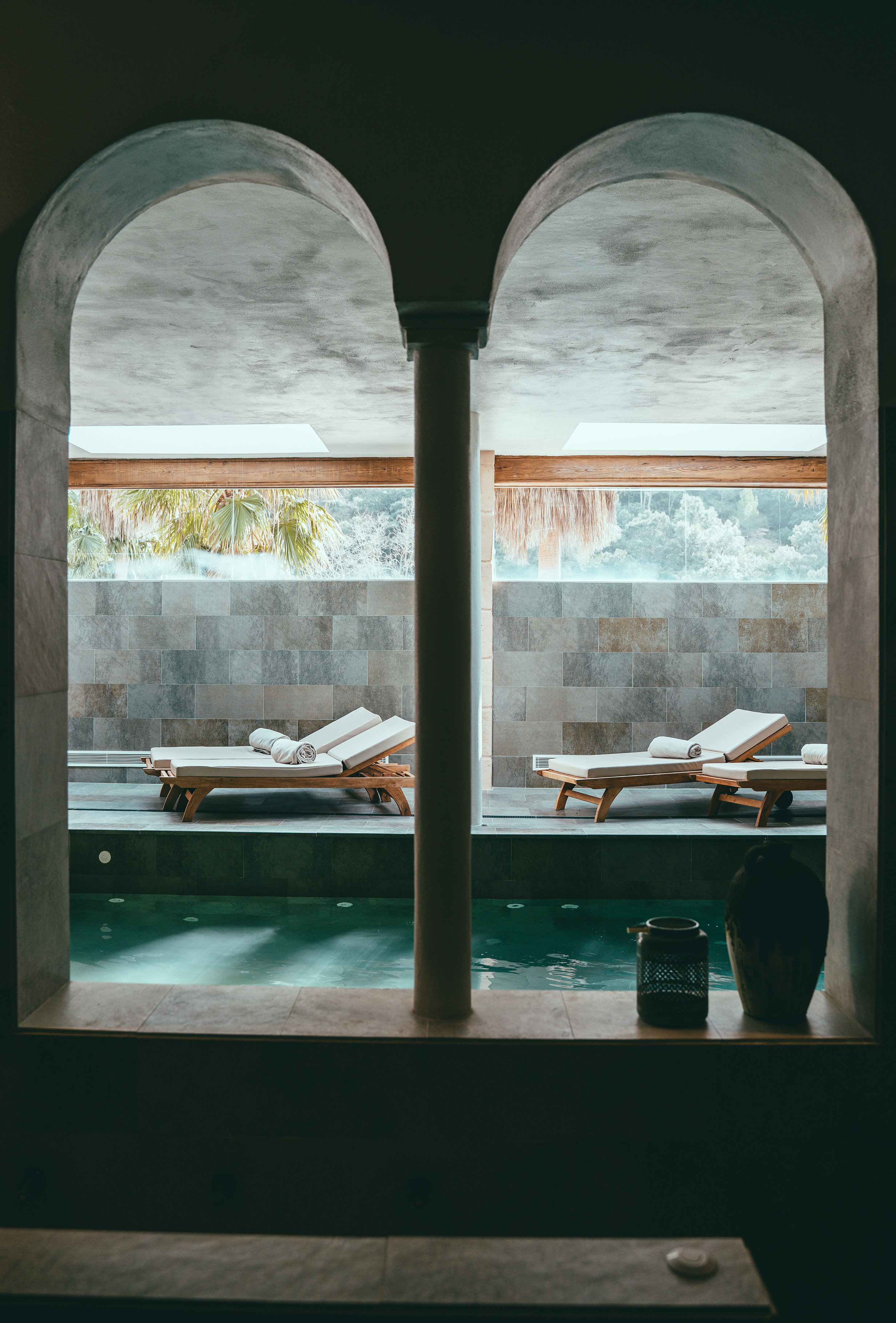 Arched view of indoor spa pool with lounge chairs and tropical outdoor scenery.