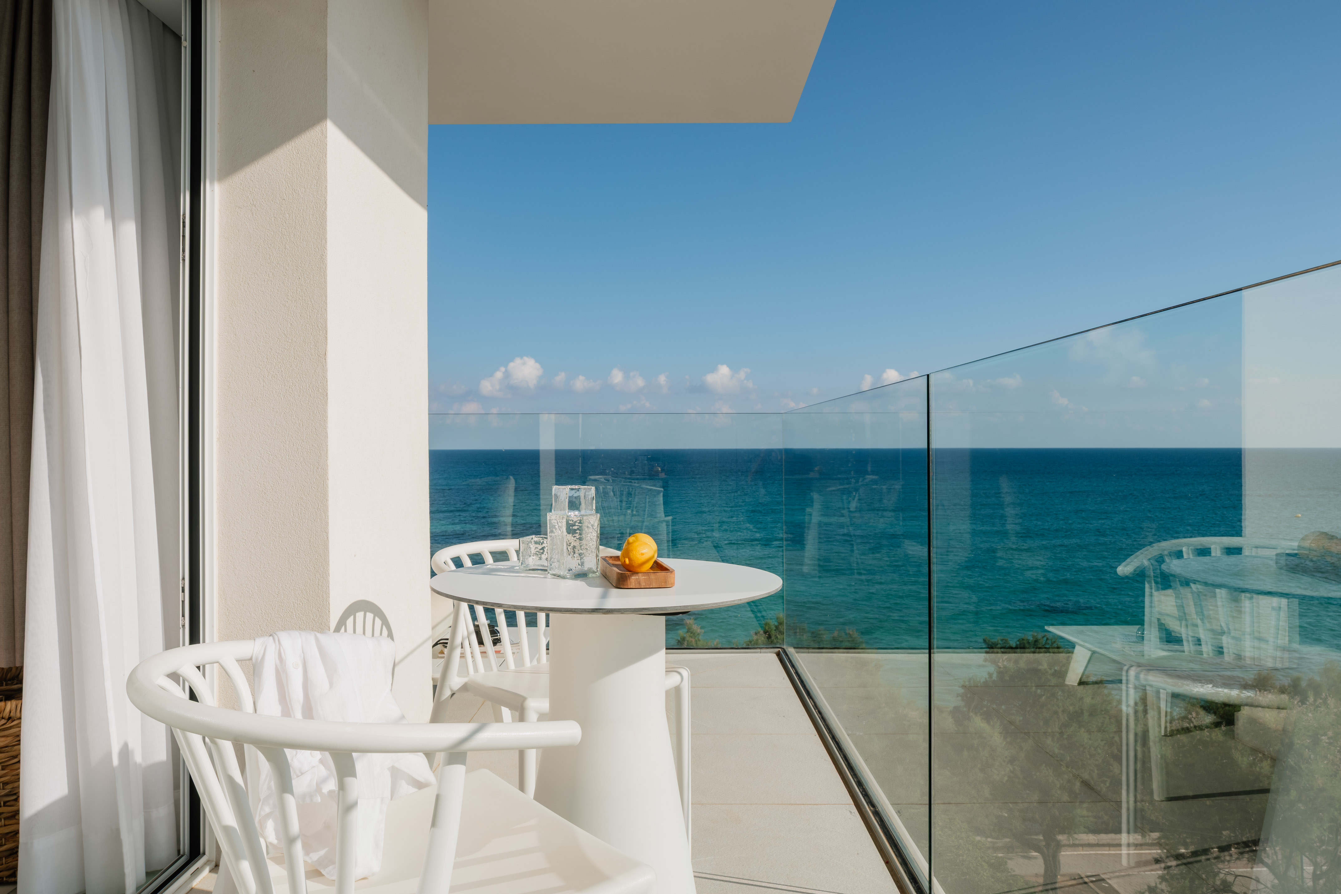 Relaxing hotel balcony with white patio furniture and panoramic ocean views.